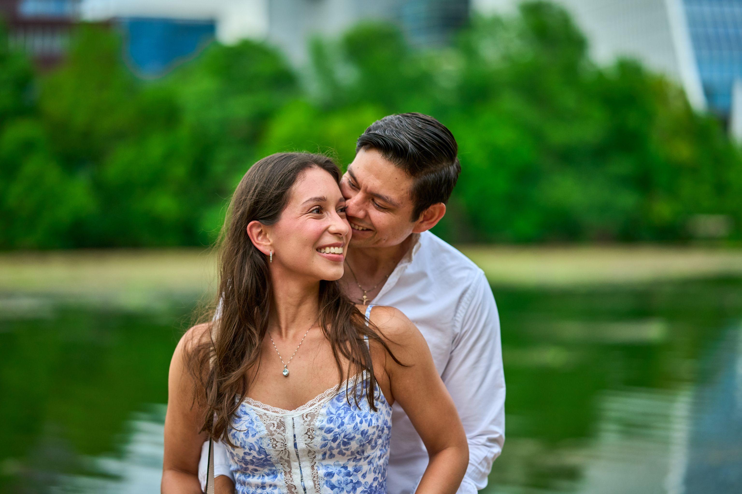 Man kissing his partner's cheek as she laughs, green park behind them — Butler Metro Park photography, Austin A man kissing his partner's cheek as she laughs, green park behind them.
