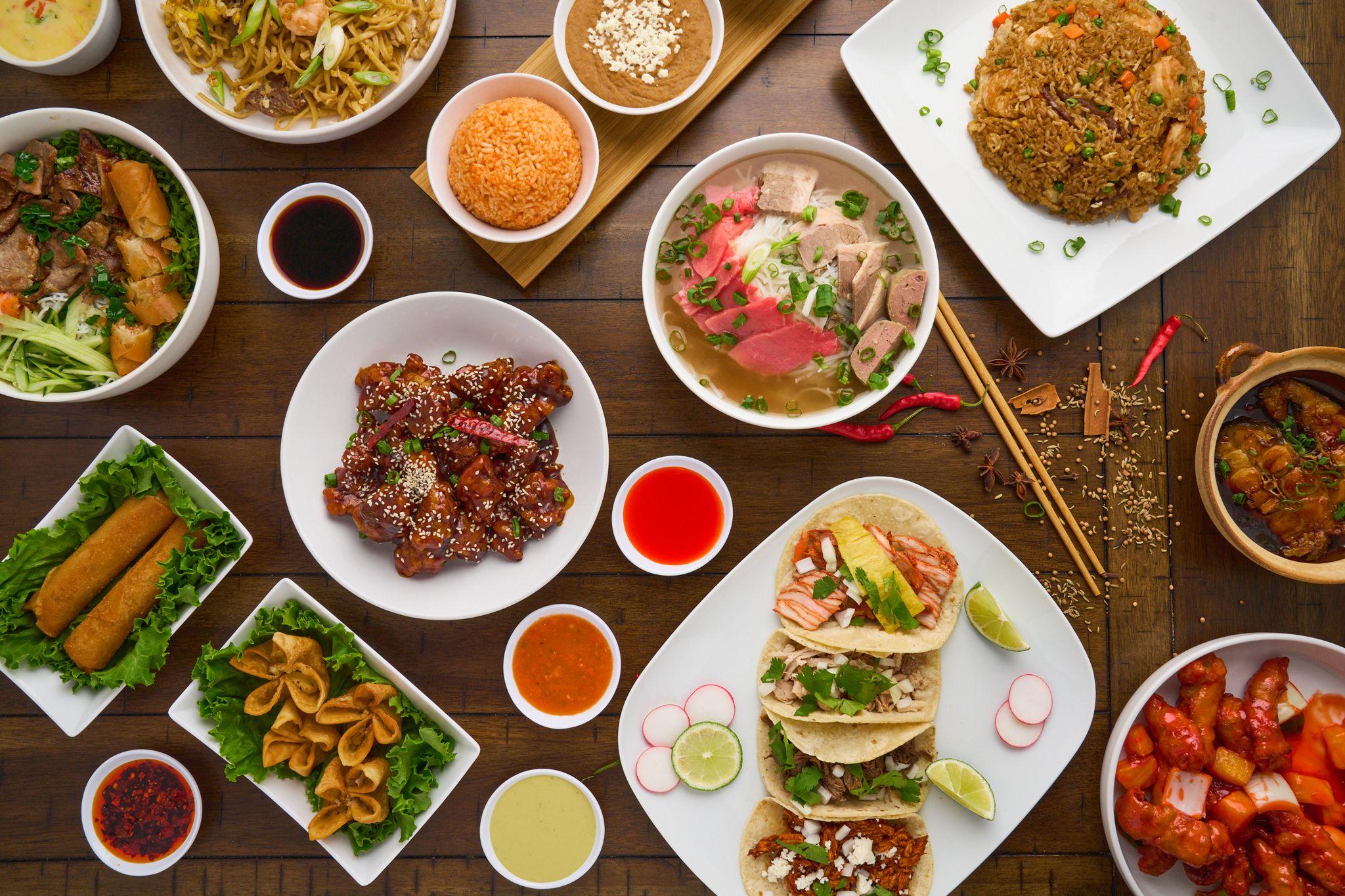 Overhead spread of Asian dishes — pho, glazed wings, tacos, spring rolls and dipping sauces — Food & restaurant photography, Austin An overhead spread of Asian dishes — pho, glazed wings, tacos, spring rolls and dipping sauces on a wooden table.