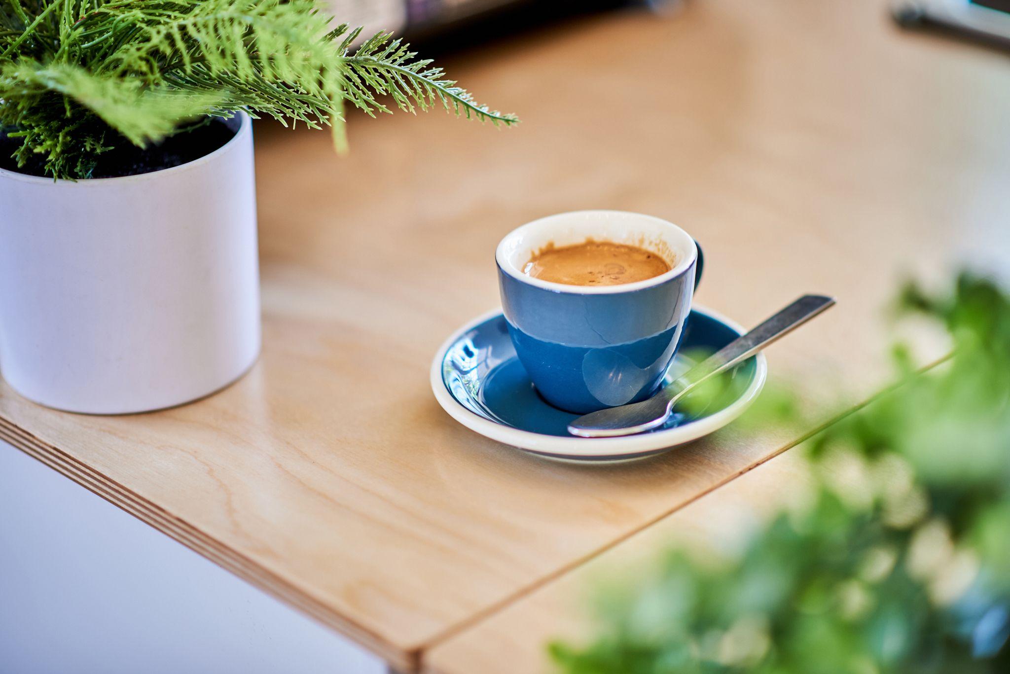 Cappuccino in a blue cup and saucer on a pale wooden table — Hospitality & leisure photography, Austin A cappuccino in a blue cup and saucer on a pale wooden table.