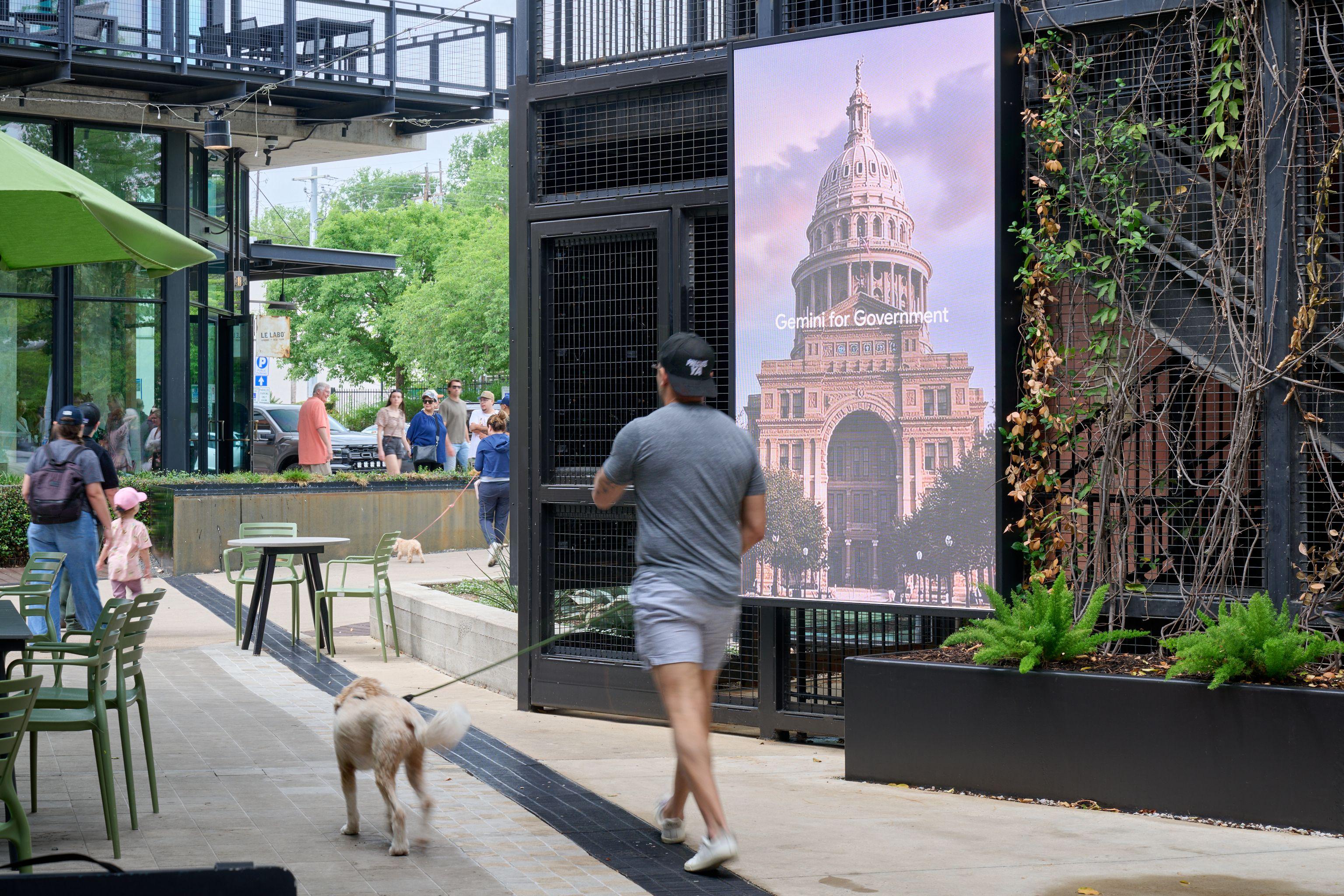 Runner and a dog passing a large backlit panel showing the Texas State Capitol — Outdoor media photography, Austin A runner and a dog passing a large backlit panel showing the Texas State Capitol.