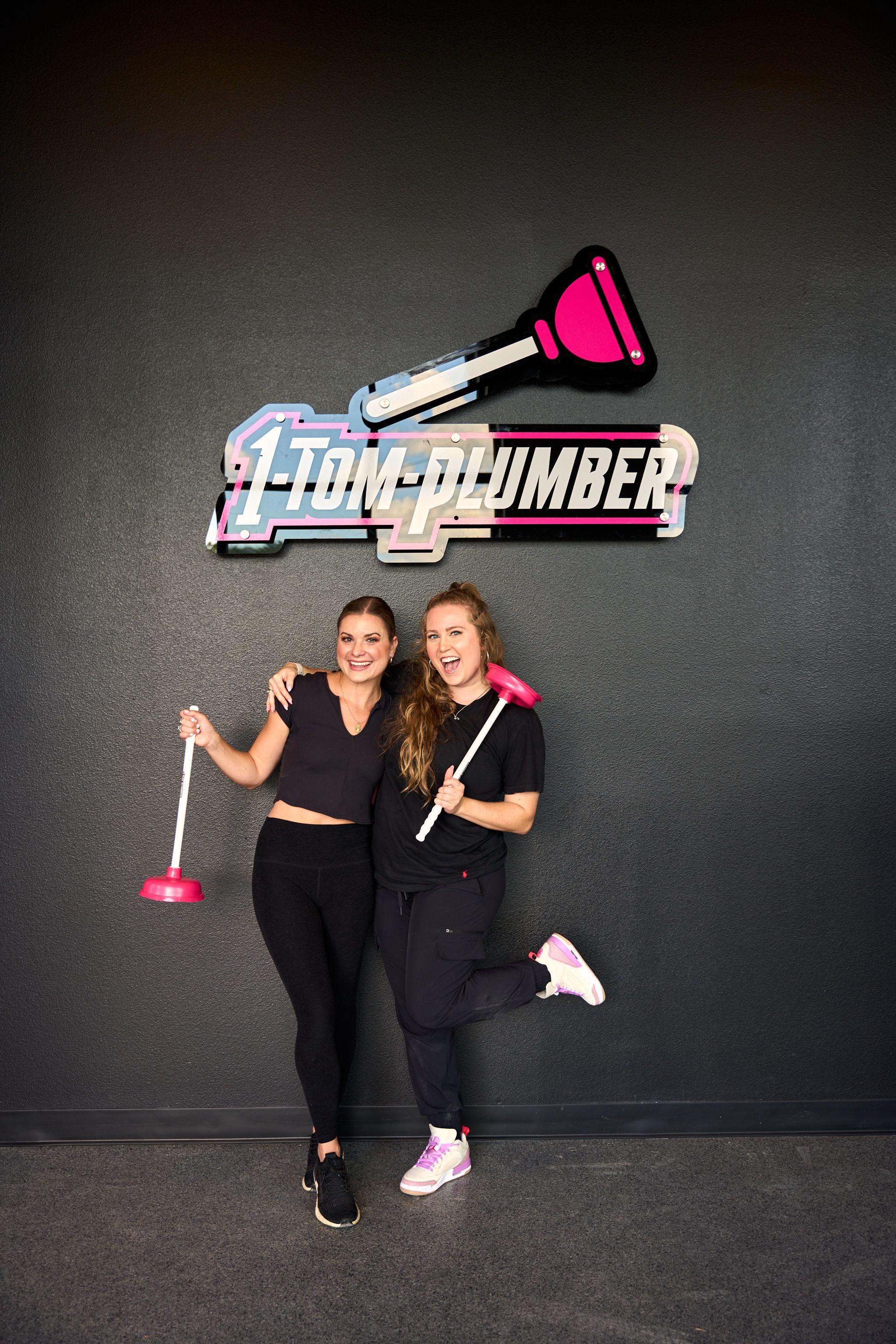 Two staffers holding plungers in front of a 1-Tom-Plumber branded backdrop — Brand activation photography, Austin Two staffers holding plungers in front of a 1-Tom-Plumber branded backdrop.
