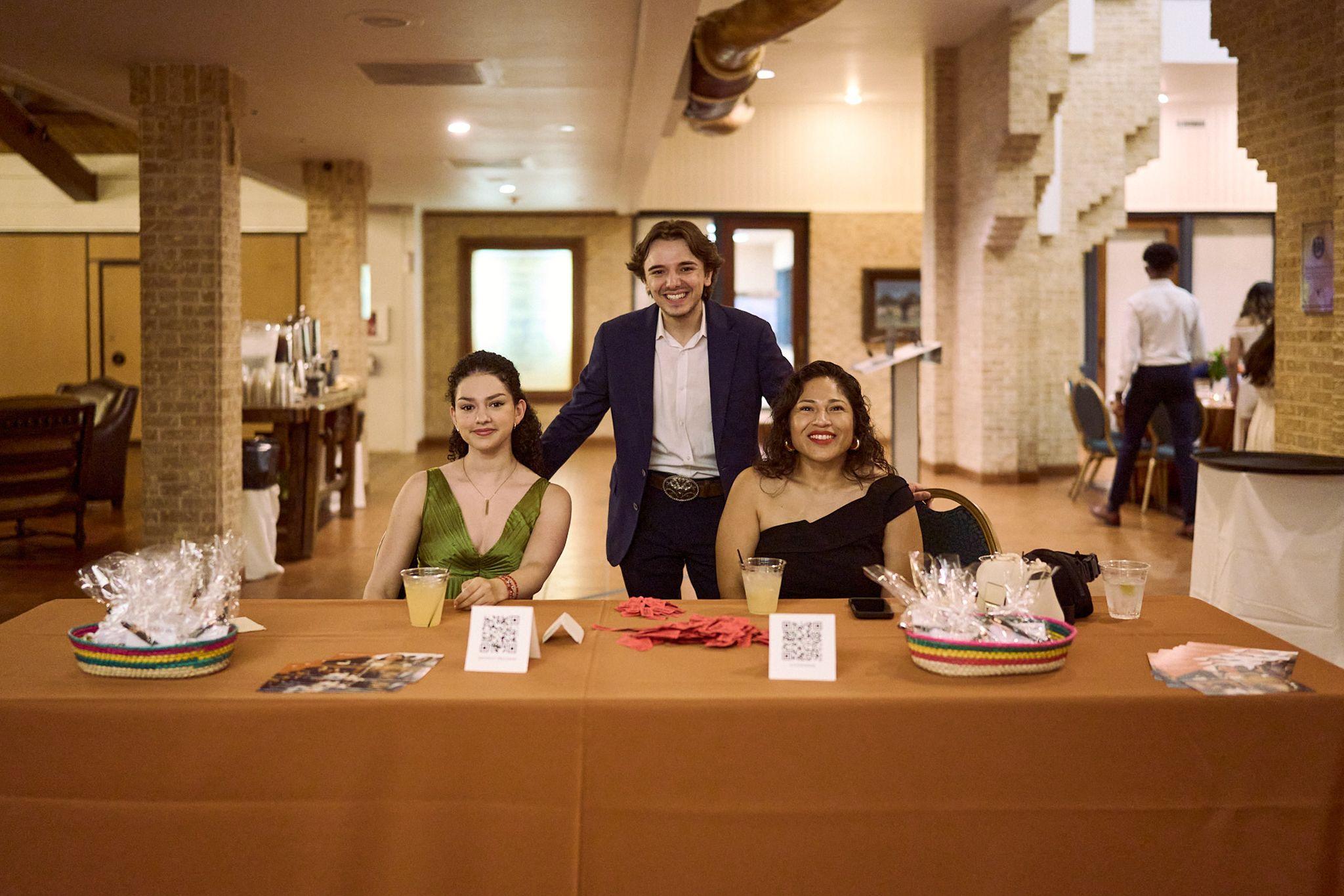 Three students standing behind a registration table at a campus event — UT Austin photography, Austin Three students standing behind a registration table at a campus event.