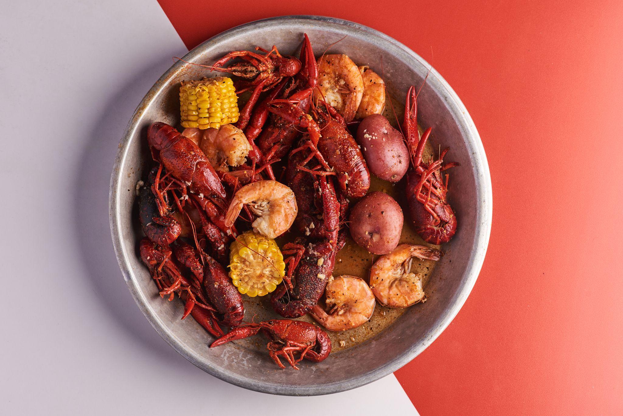 Seafood boil of crawfish, shrimp, corn and potatoes in a metal pan on a red background — Food & restaurant photography, Austin A seafood boil of crawfish, shrimp, corn and potatoes in a metal pan on a red background.