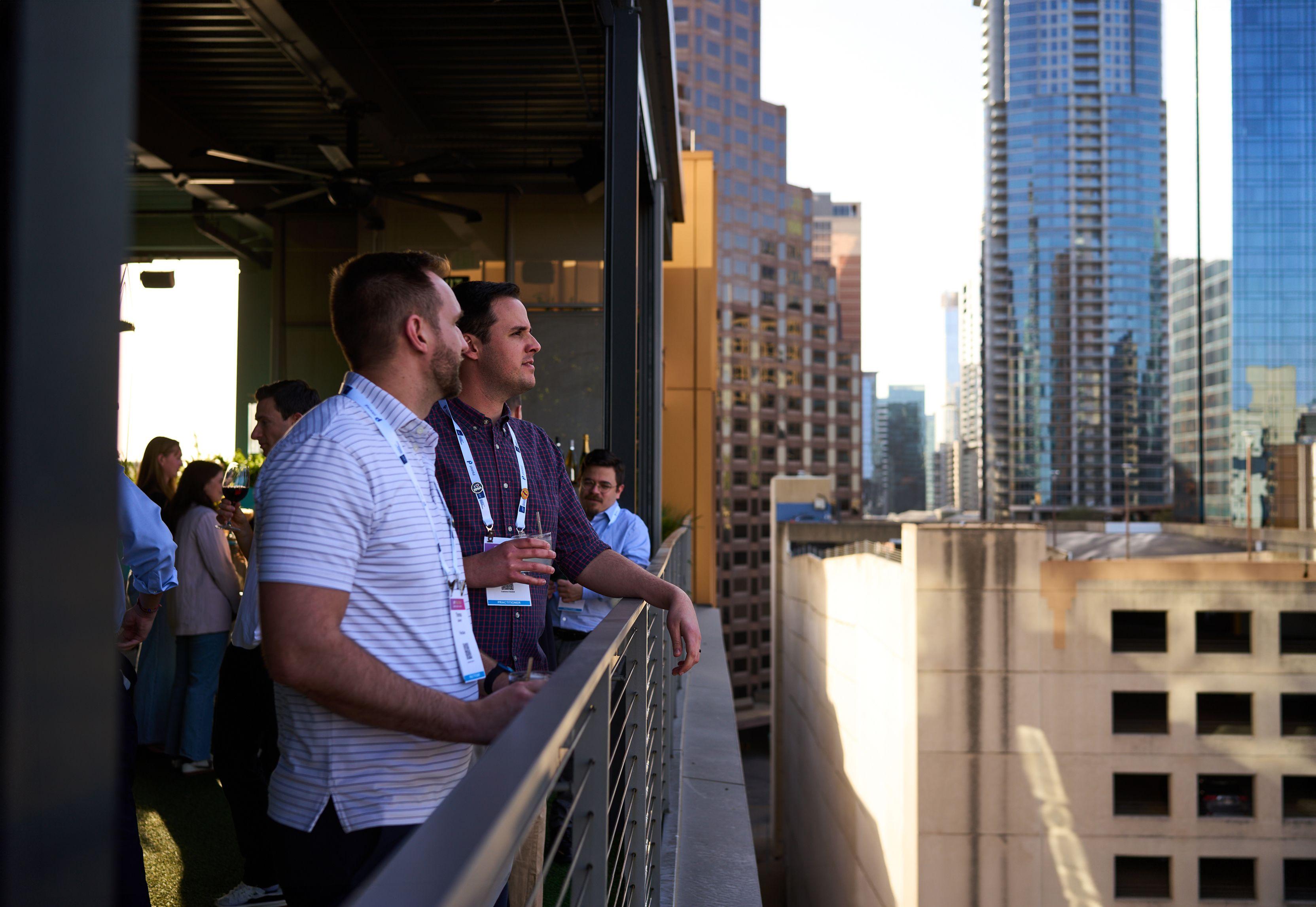 Two colleagues with lanyards leaning on a rooftop railing above the downtown Austin skyline — Business Parties photography, Austin Two colleagues with lanyards leaning on a rooftop railing above the downtown Austin skyline.