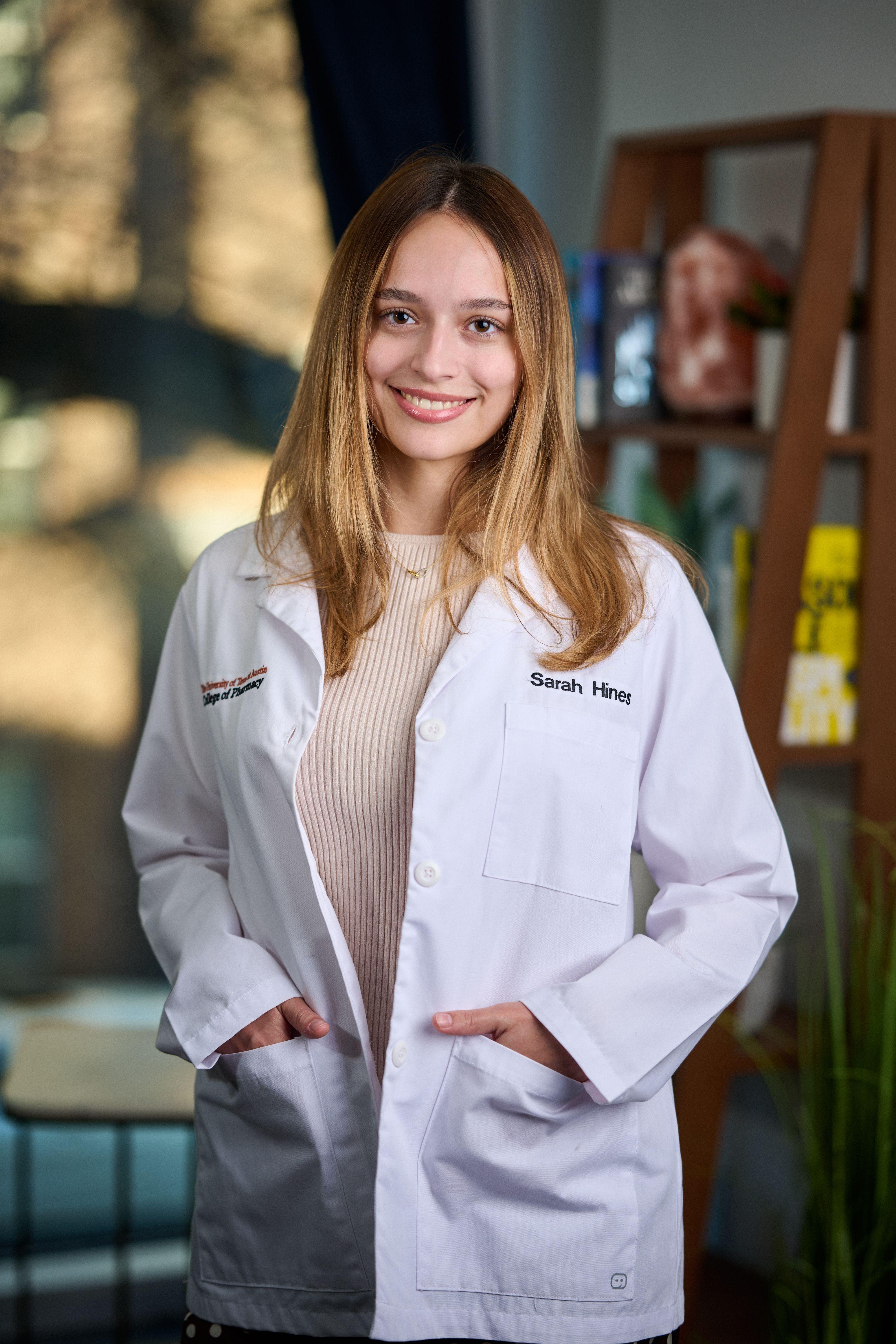 Student in a white lab coat with an embroidered name standing in a college interior — Medical team photography, Austin Student in a white lab coat with an embroidered name standing in a college interior