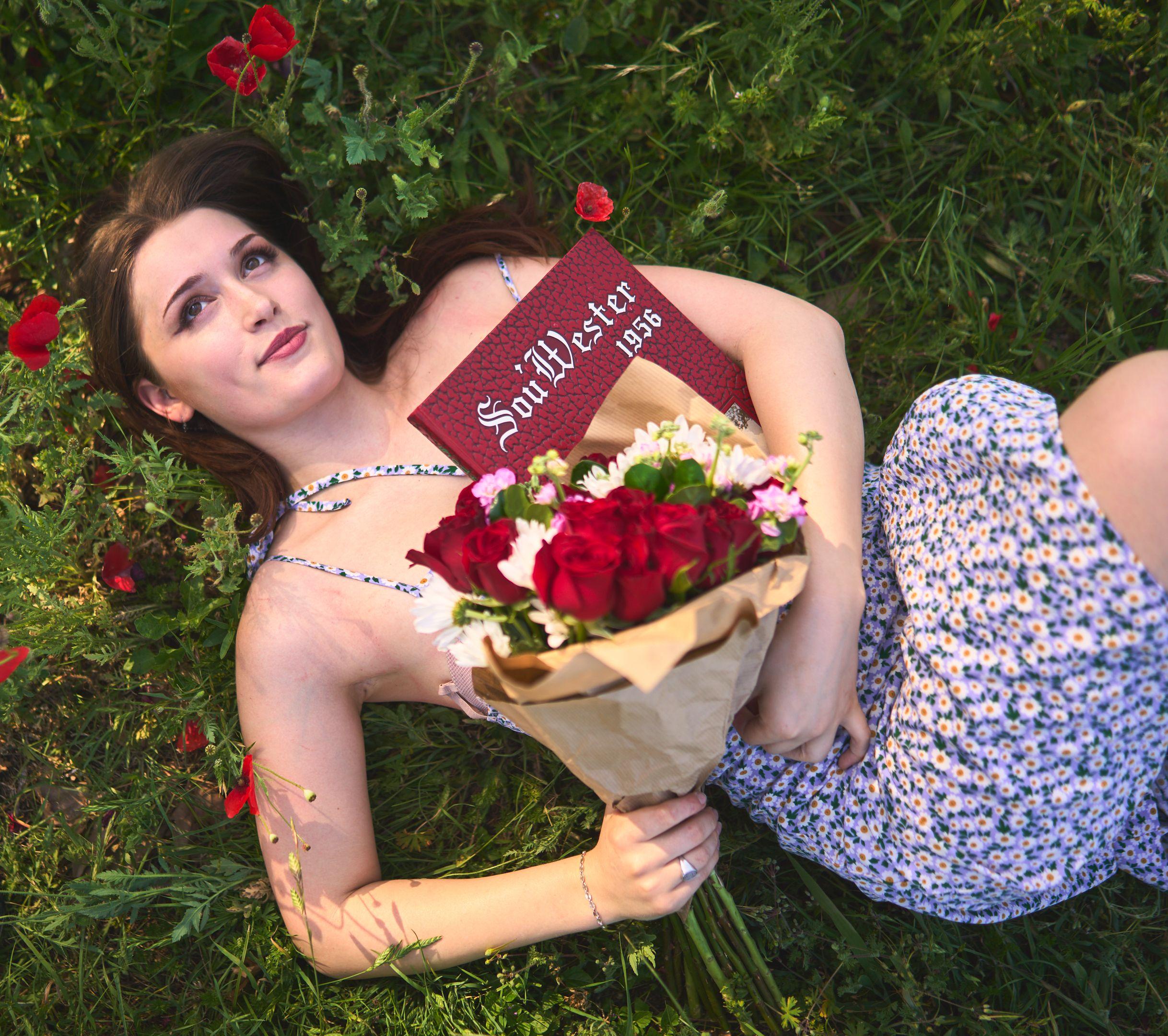 Graduate lying in the grass with a Southwestern diploma folder and a bouquet of red roses — Seasonal Wildflower Season in Texas photography, Austin A graduate lying in the grass with a Southwestern diploma folder and a bouquet of red roses.