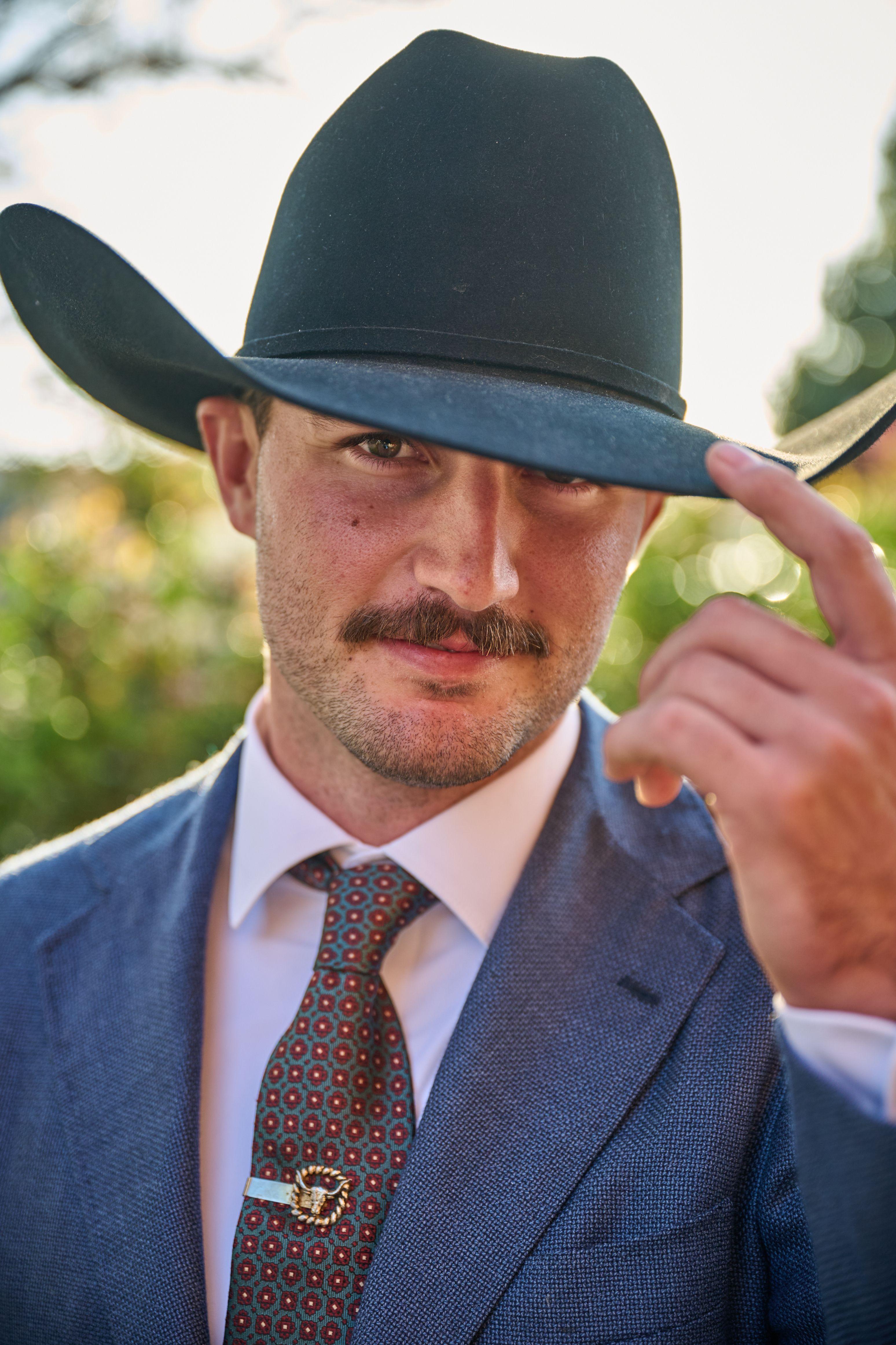 Groom in a blue suit tipping the brim of his black cowboy hat — Weddings photography, Austin A groom in a blue suit tipping the brim of his black cowboy hat.