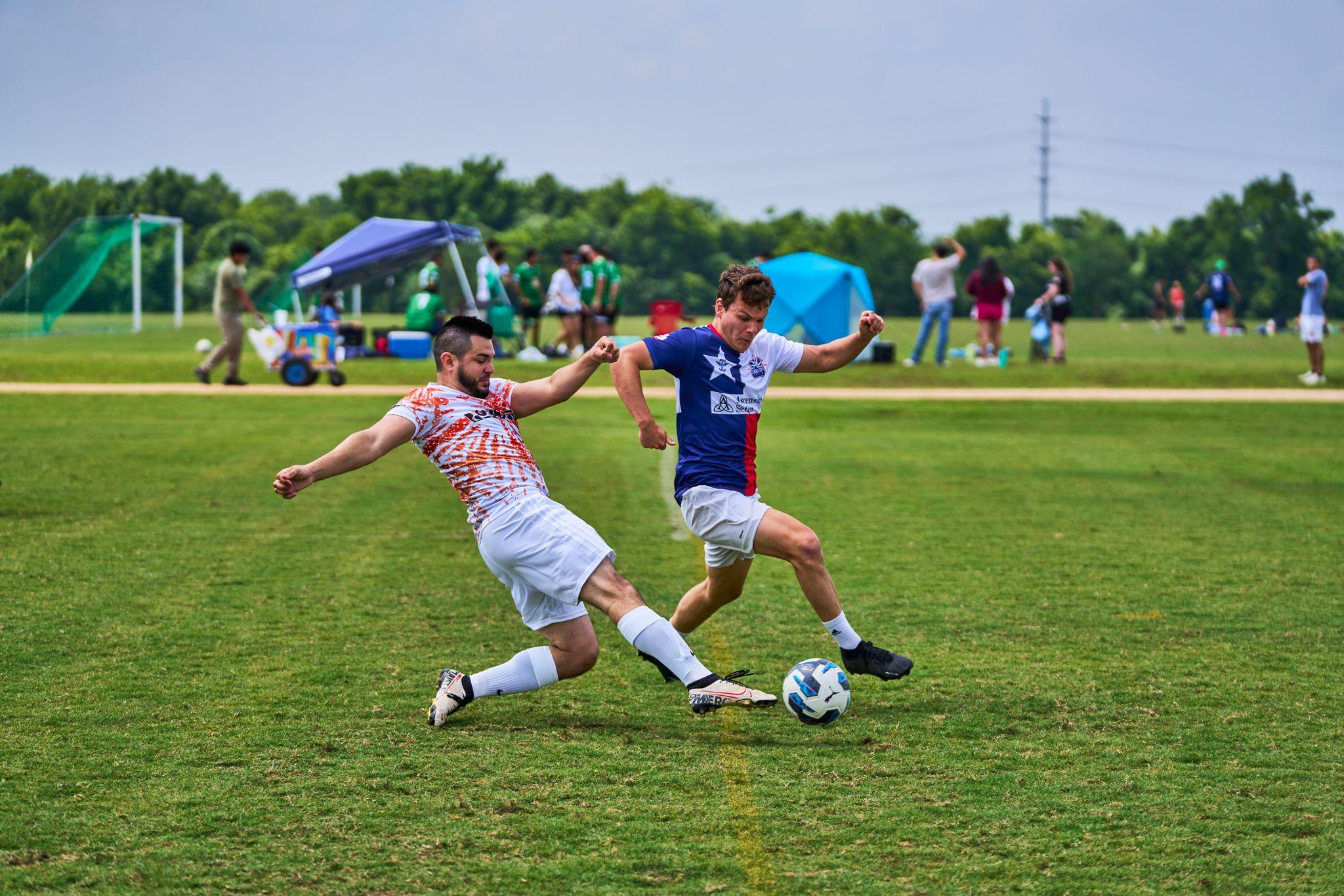 Two adult league footballers competing for the ball, one sliding in as the other shields it — Sports photography, Austin Two adult league footballers competing for the ball, one sliding in as the other shields it
