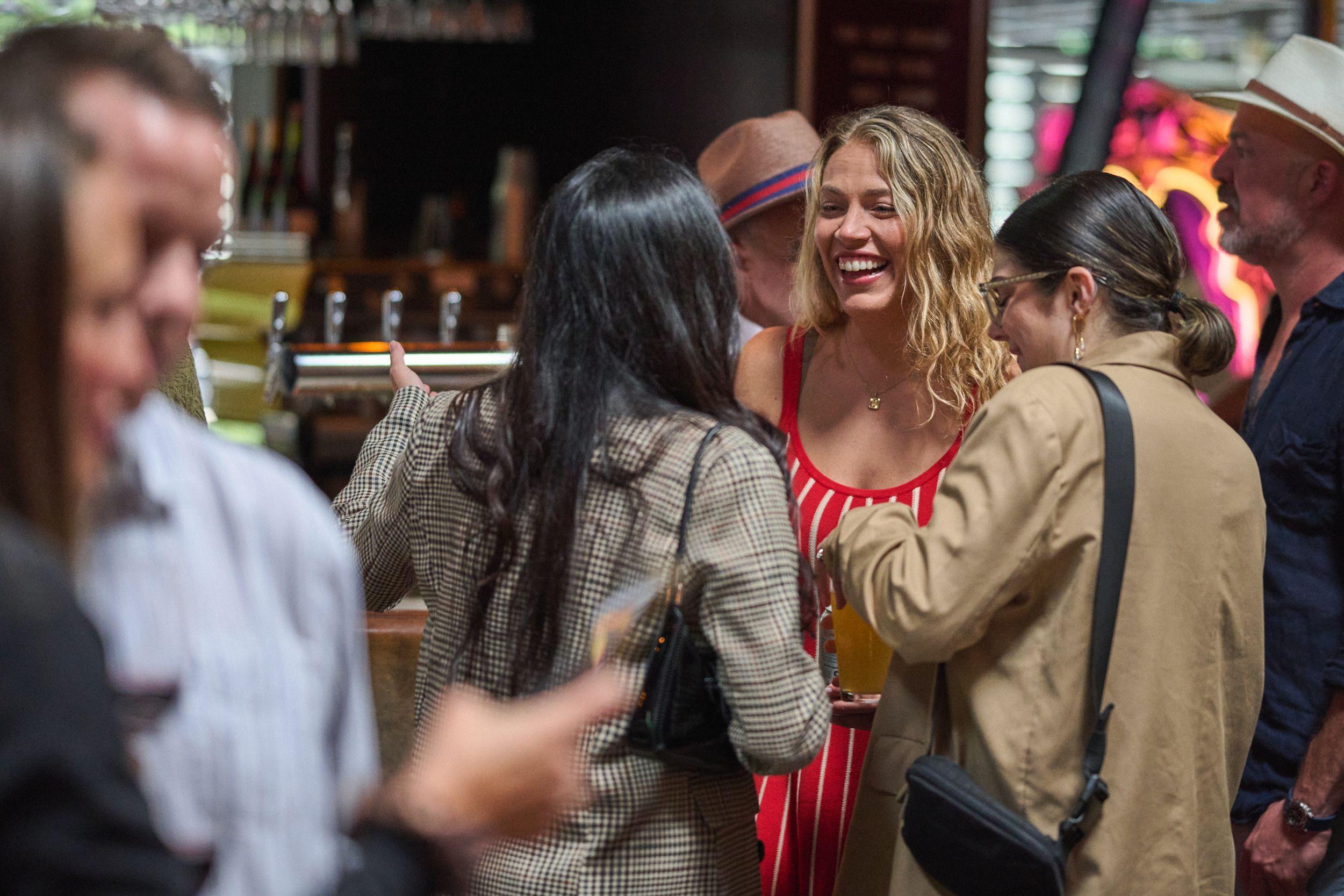 Two guests greeting each other with a laugh across a crowded bar — Business Parties photography, Austin Two guests greeting each other with a laugh across a crowded bar.