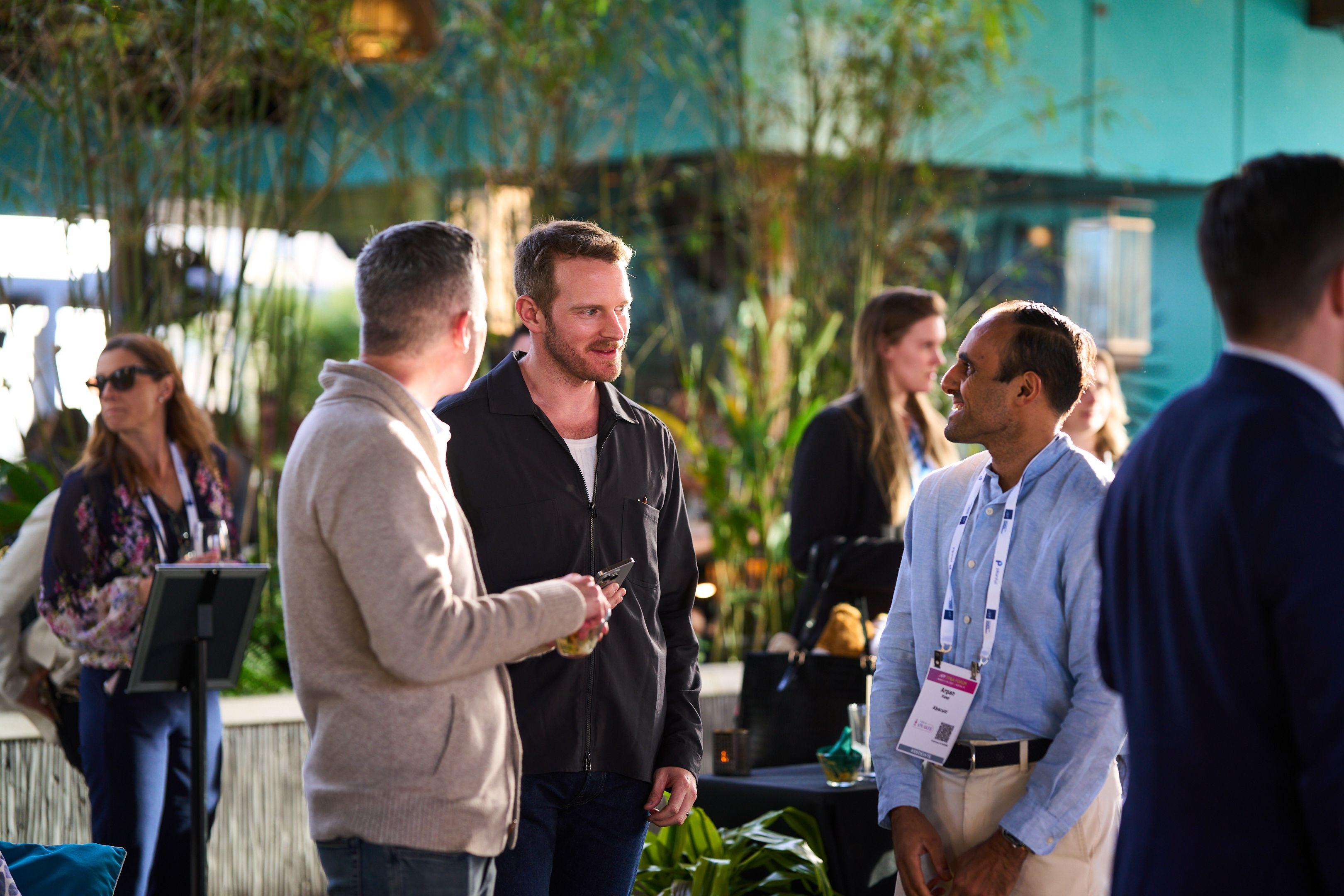 Two men in conversation holding drinks on a plant-filled rooftop patio — Business Parties photography, Austin Two men in conversation holding drinks on a plant-filled rooftop patio.