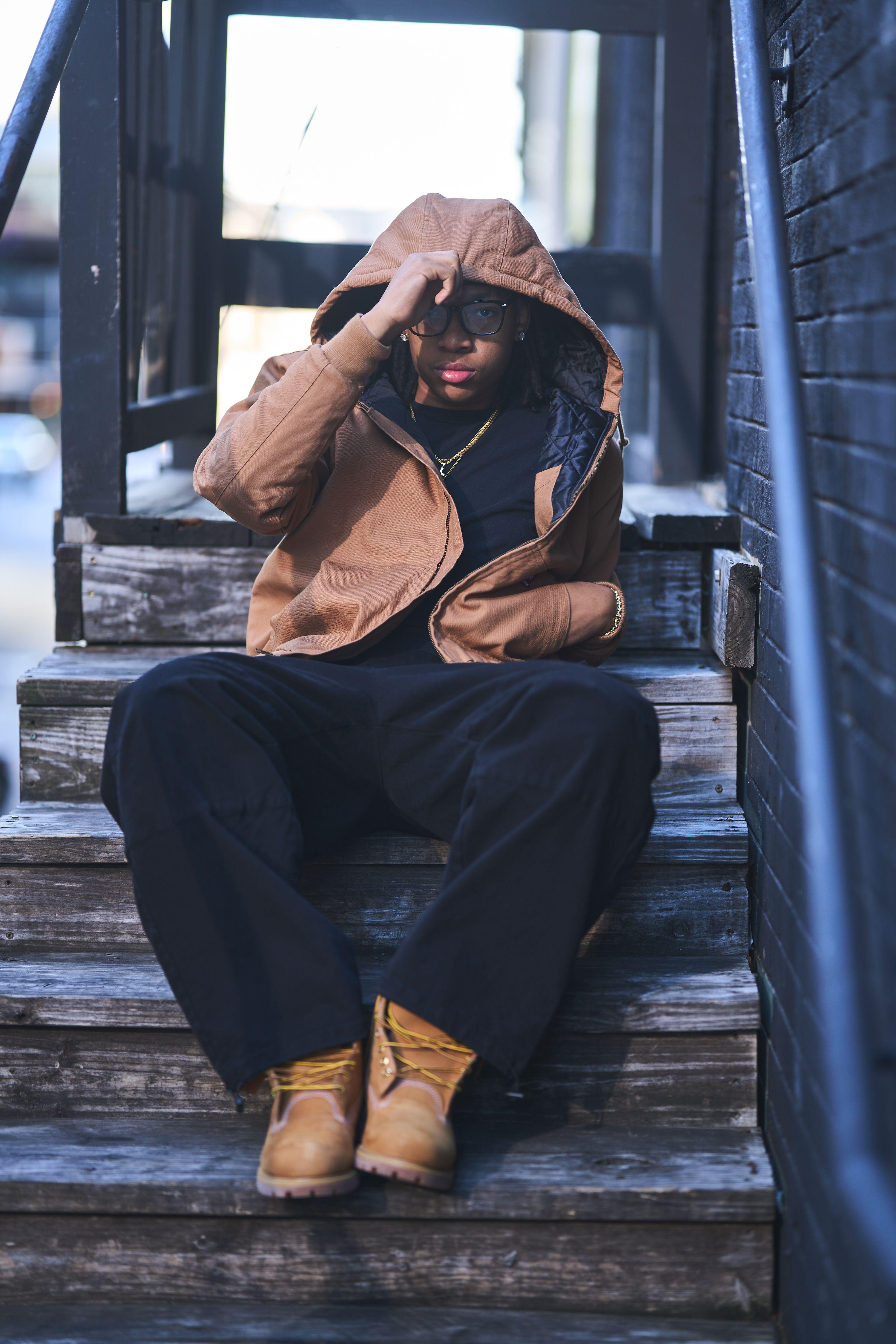 Model in a tan hooded jacket sitting on wooden steps with the hood pulled down over his face — Fashion & editorial photography, Austin A model in a tan hooded jacket sitting on wooden steps with the hood pulled down over his face.