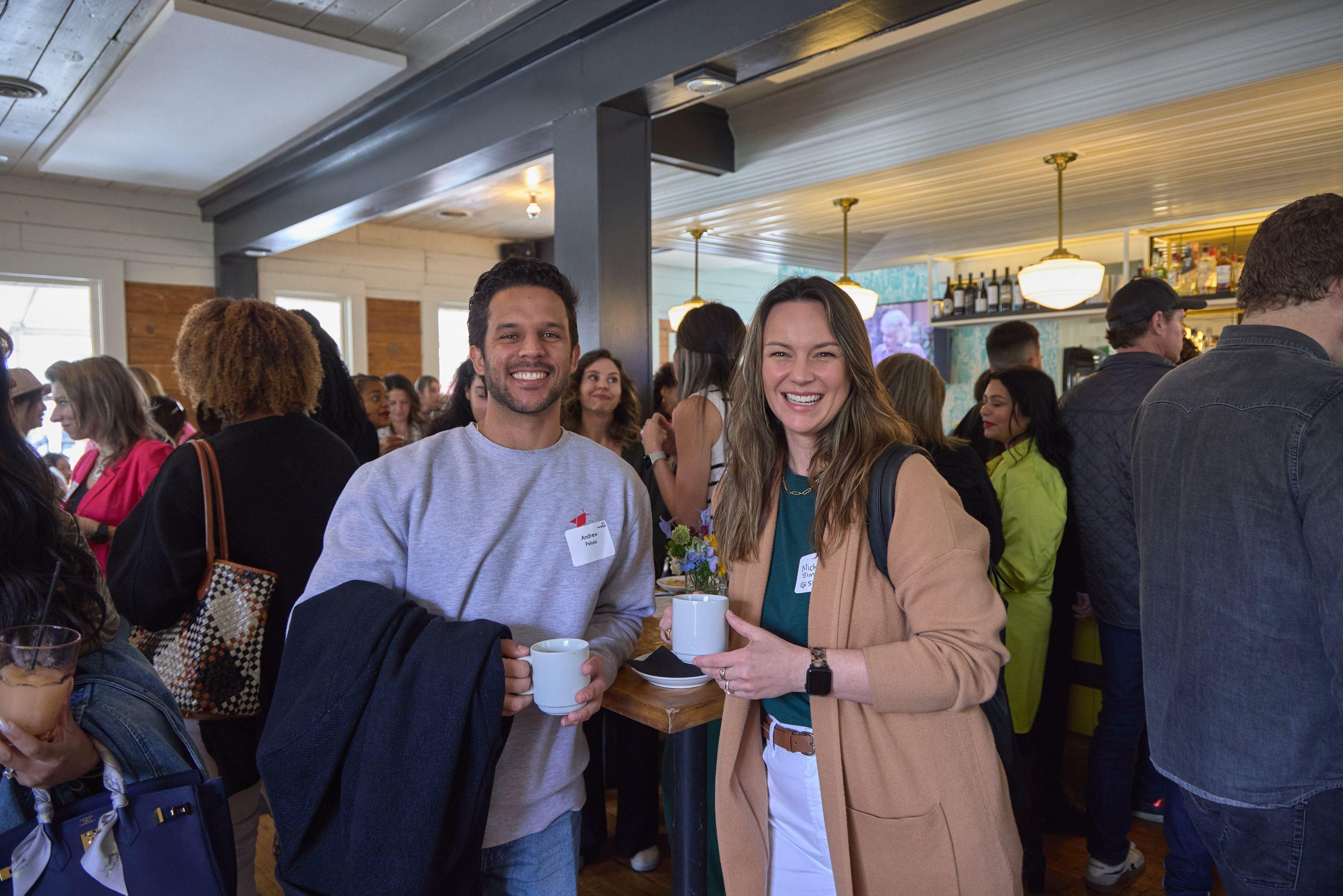 Pair of guests holding coffee cups and smiling at a daytime networking reception — Business Parties photography, Austin A pair of guests holding coffee cups and smiling at a daytime networking reception.