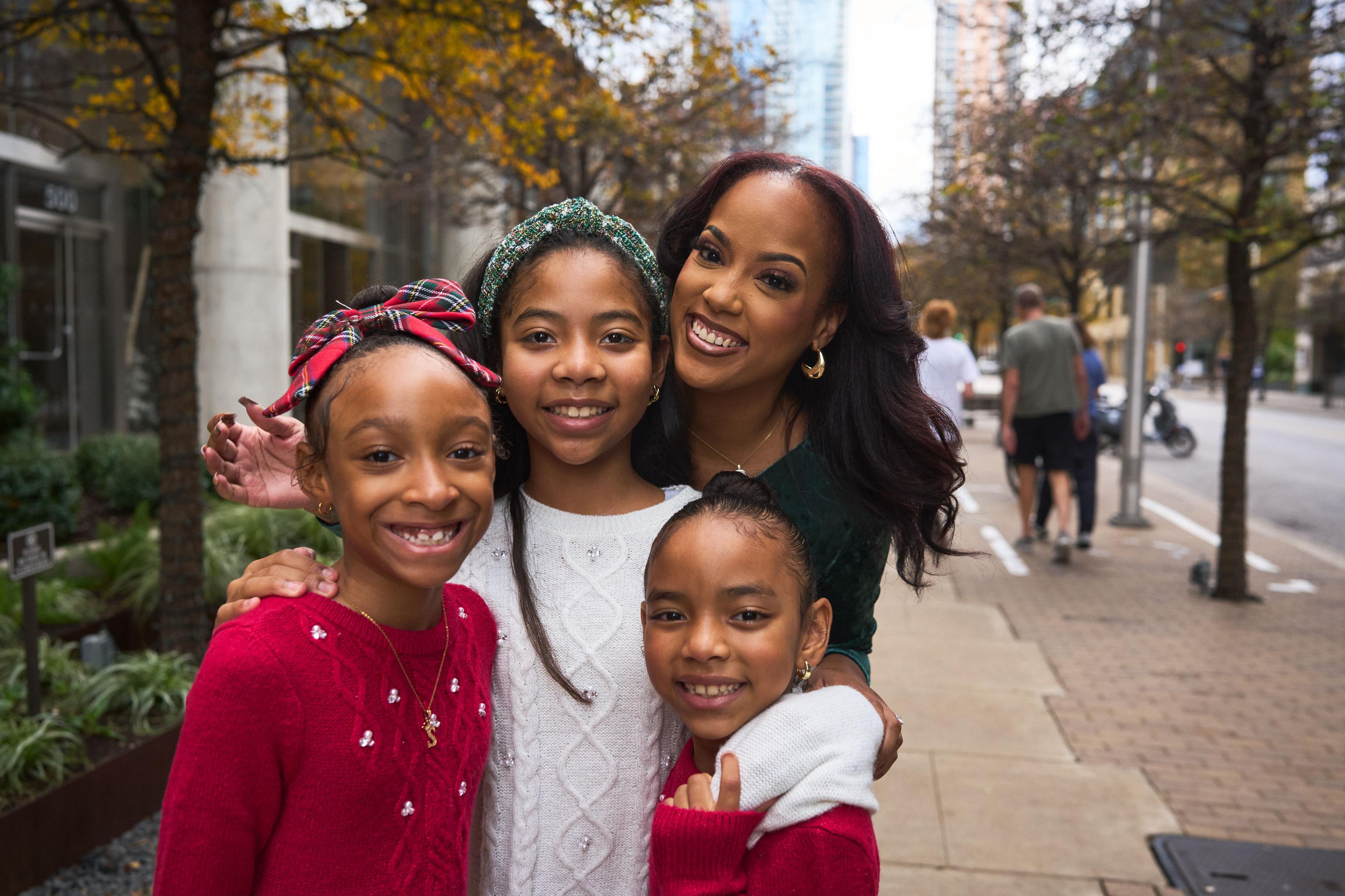 Mother and three daughters in festive knitwear leaning together on a downtown street — Seasonal Christmas & Fall photography, Austin A mother and three daughters in festive knitwear leaning together on a downtown street.