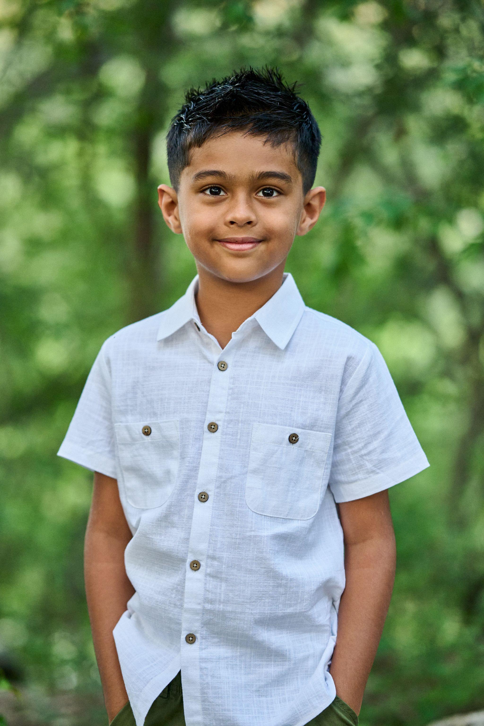 Boy in a white shirt smiling against deep green foliage at Bull Creek — Bull Creek District Park photography, Austin A boy in a white shirt smiling against deep green foliage at Bull Creek