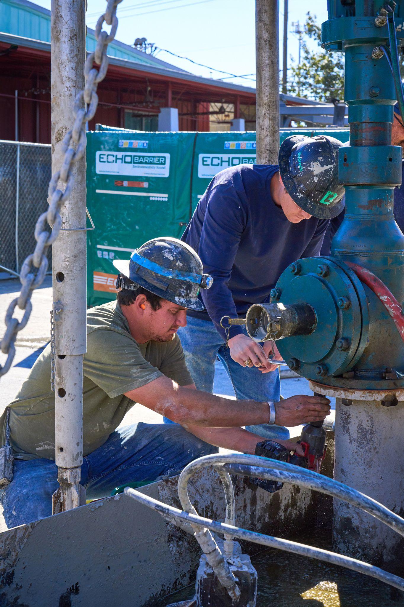 Two workers in hard hats and welding masks fitting a large valve on a pipe stack at a job site — Industrial photography, Austin Two workers in hard hats and welding masks fitting a large valve on a pipe stack at a job site