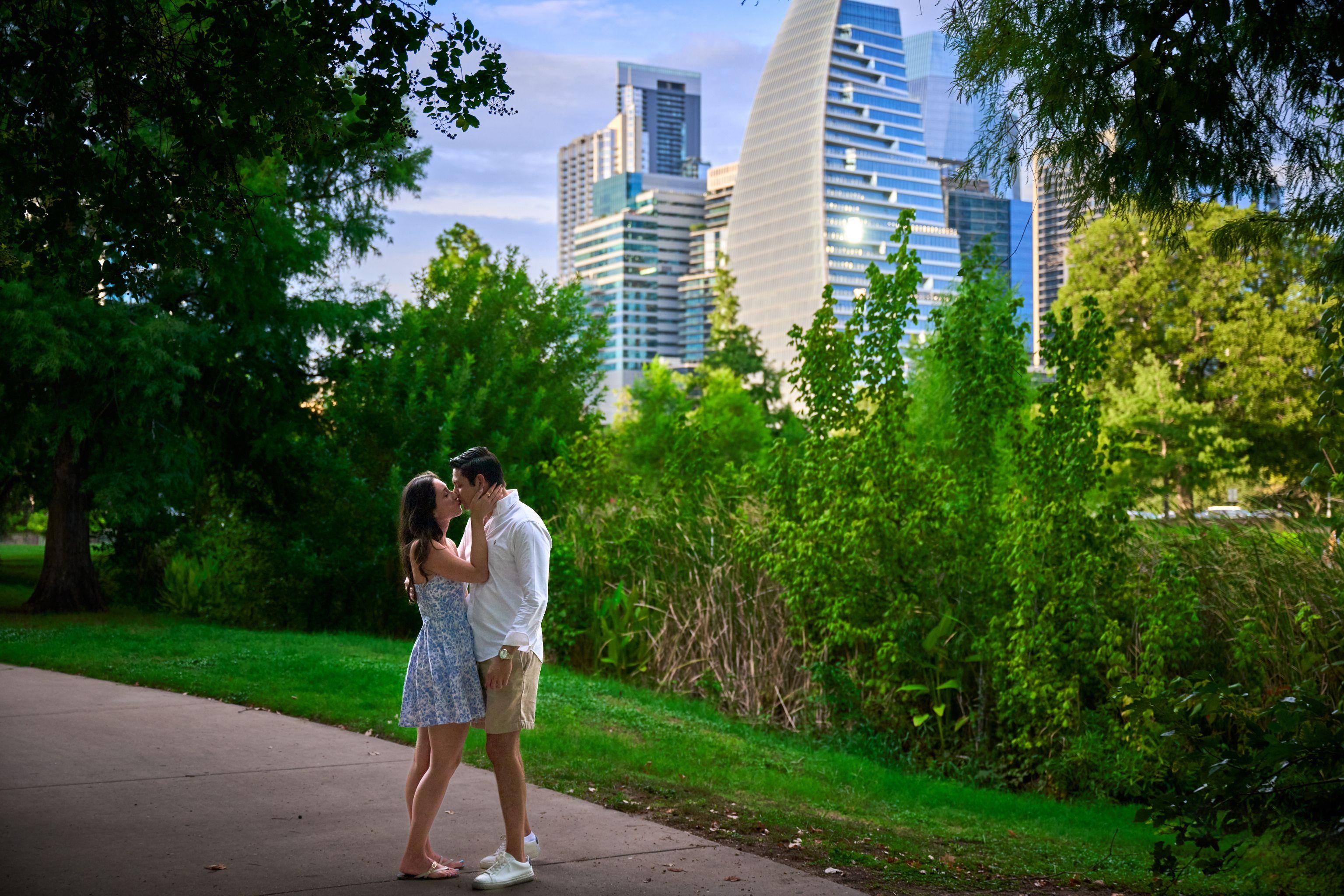 Couple embracing on a green path with the downtown Austin skyline framed by trees — Engagement & Proposals photography, Austin A couple embracing on a green path with the downtown Austin skyline framed by trees.