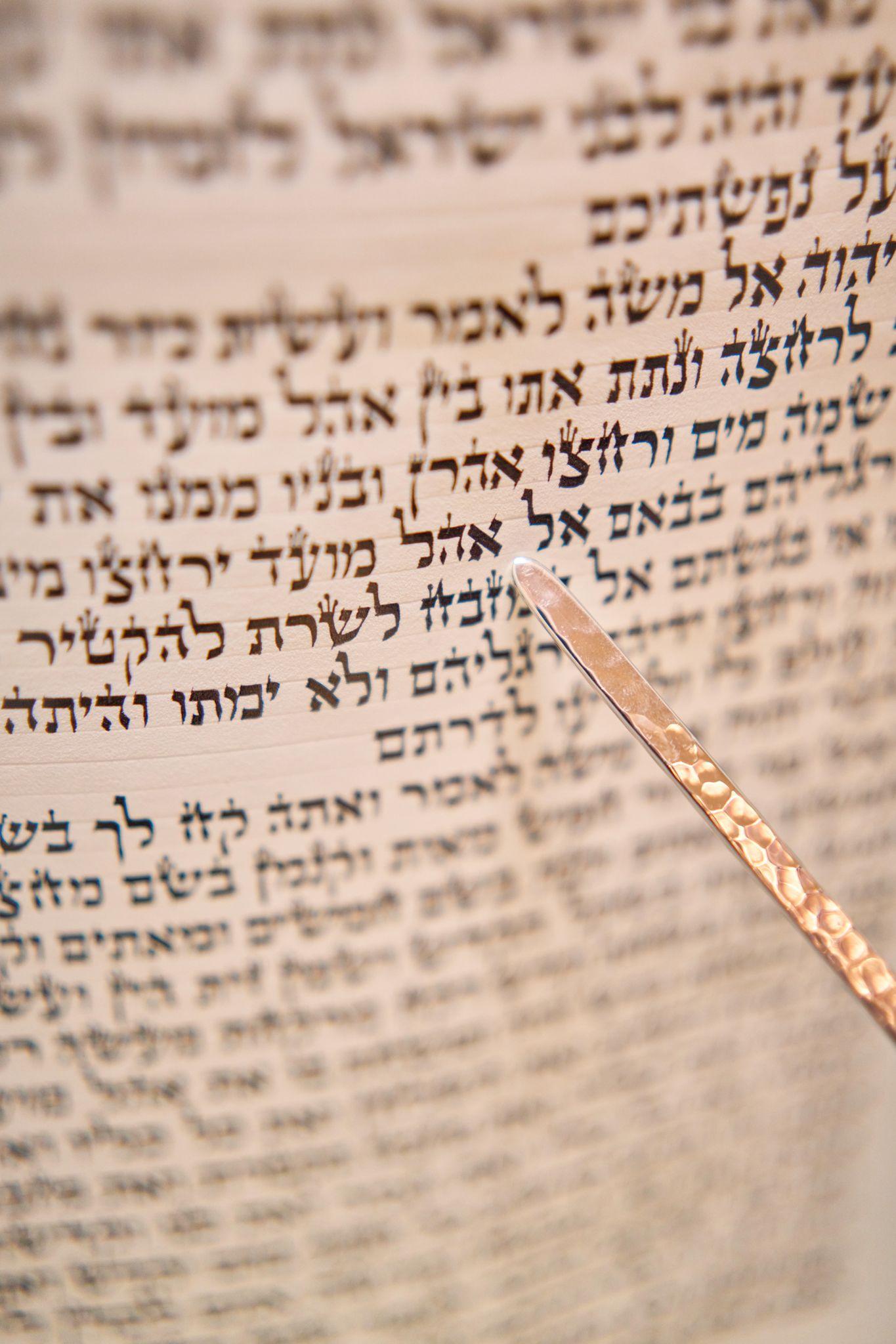 Close view of a Torah scroll's Hebrew lettering with a silver yad resting on the parchment — Religious Ceremonies photography, Austin A close view of a Torah scroll's Hebrew lettering with a silver yad resting on the parchment.
