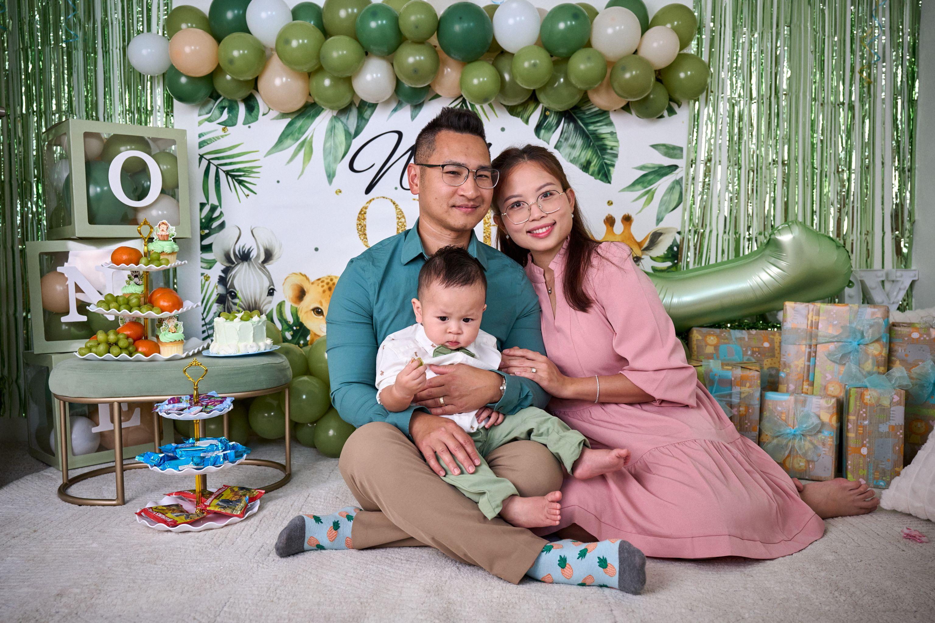 Parents sitting on the floor with their baby in front of a jungle-themed first birthday set — Mobile photo studio, Austin Parents sitting on the floor with their baby in front of a jungle-themed first birthday set, balloon arch and cake table built into a living room