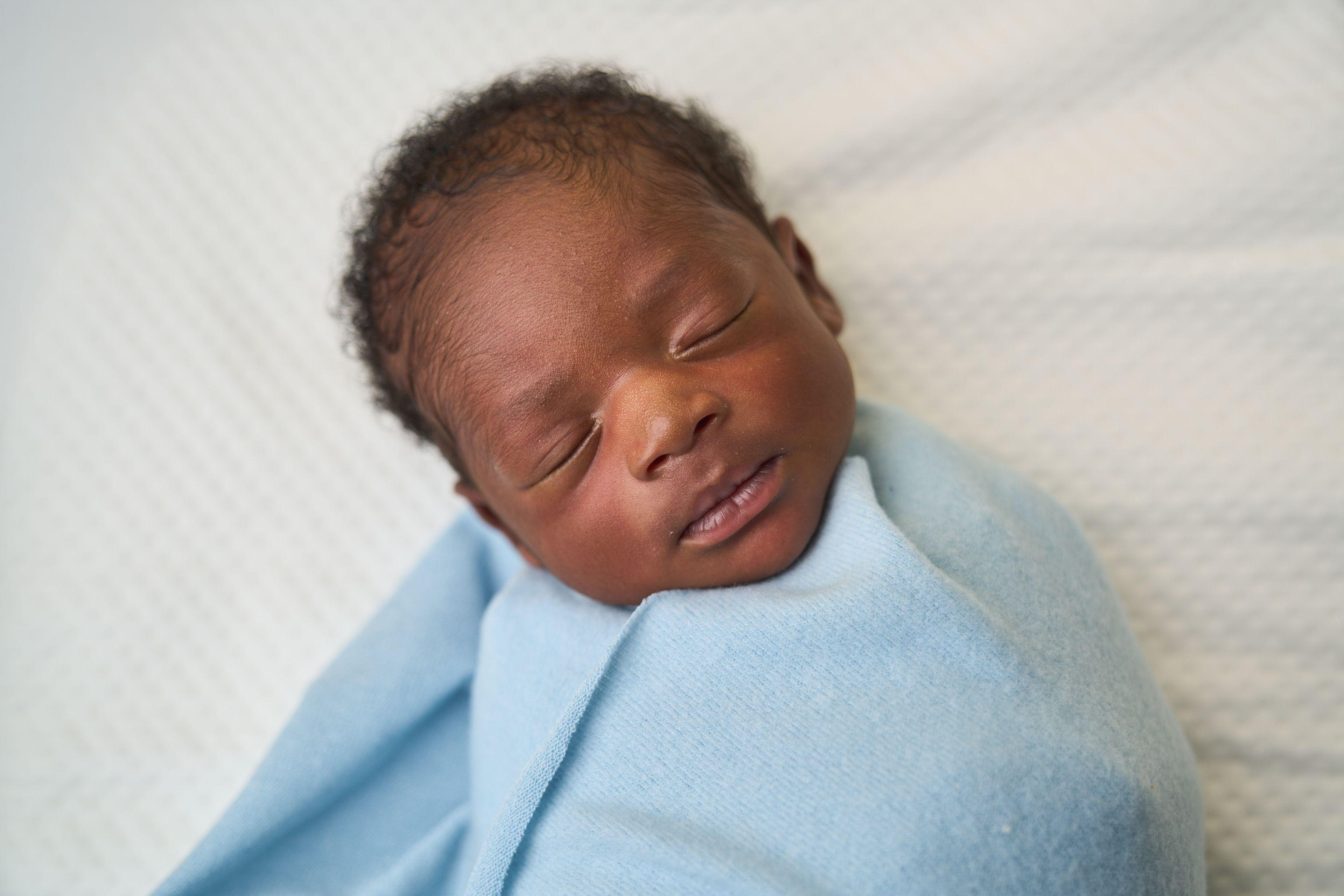 Newborn wrapped in blue, asleep with one cheek against the blanket — Newborn photography, Austin A newborn wrapped in blue, asleep with one cheek against the blanket.