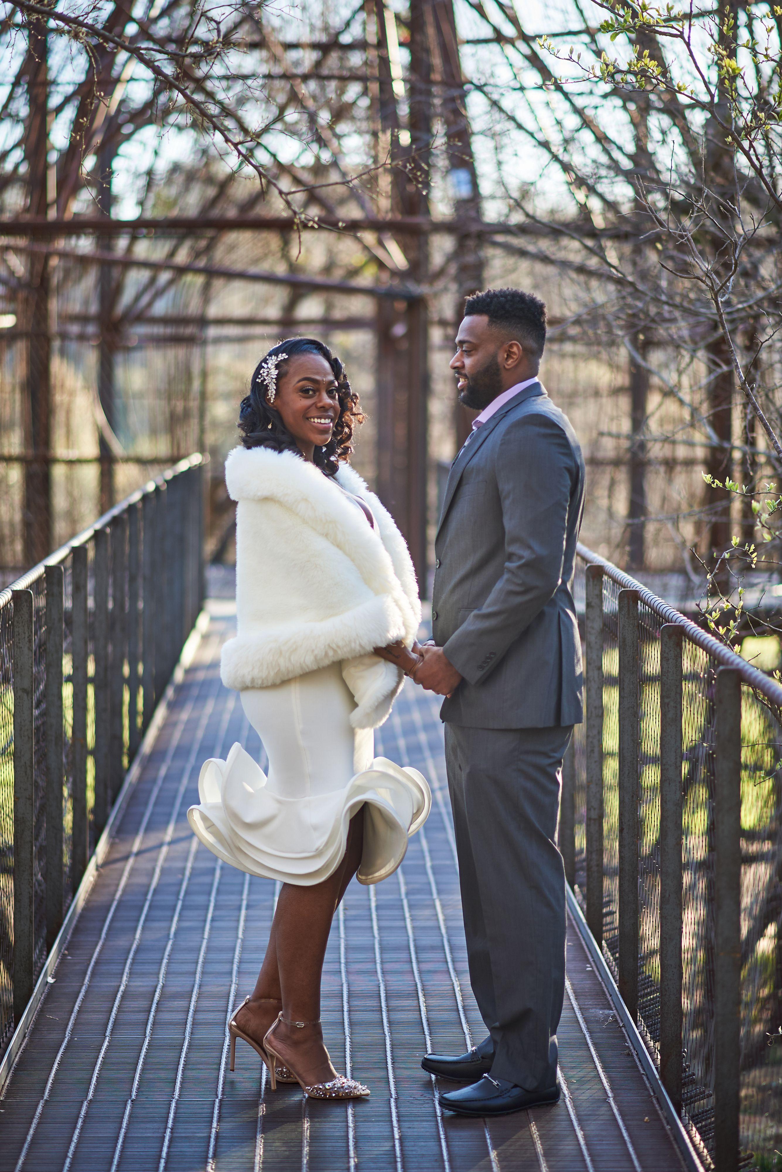 Woman in a white fur coat swinging round on the black metal footbridge in Pease Park with a man — Pease Park photography, Austin A woman in a white fur coat swinging round on the black metal footbridge in Pease Park with a man in a gray suit