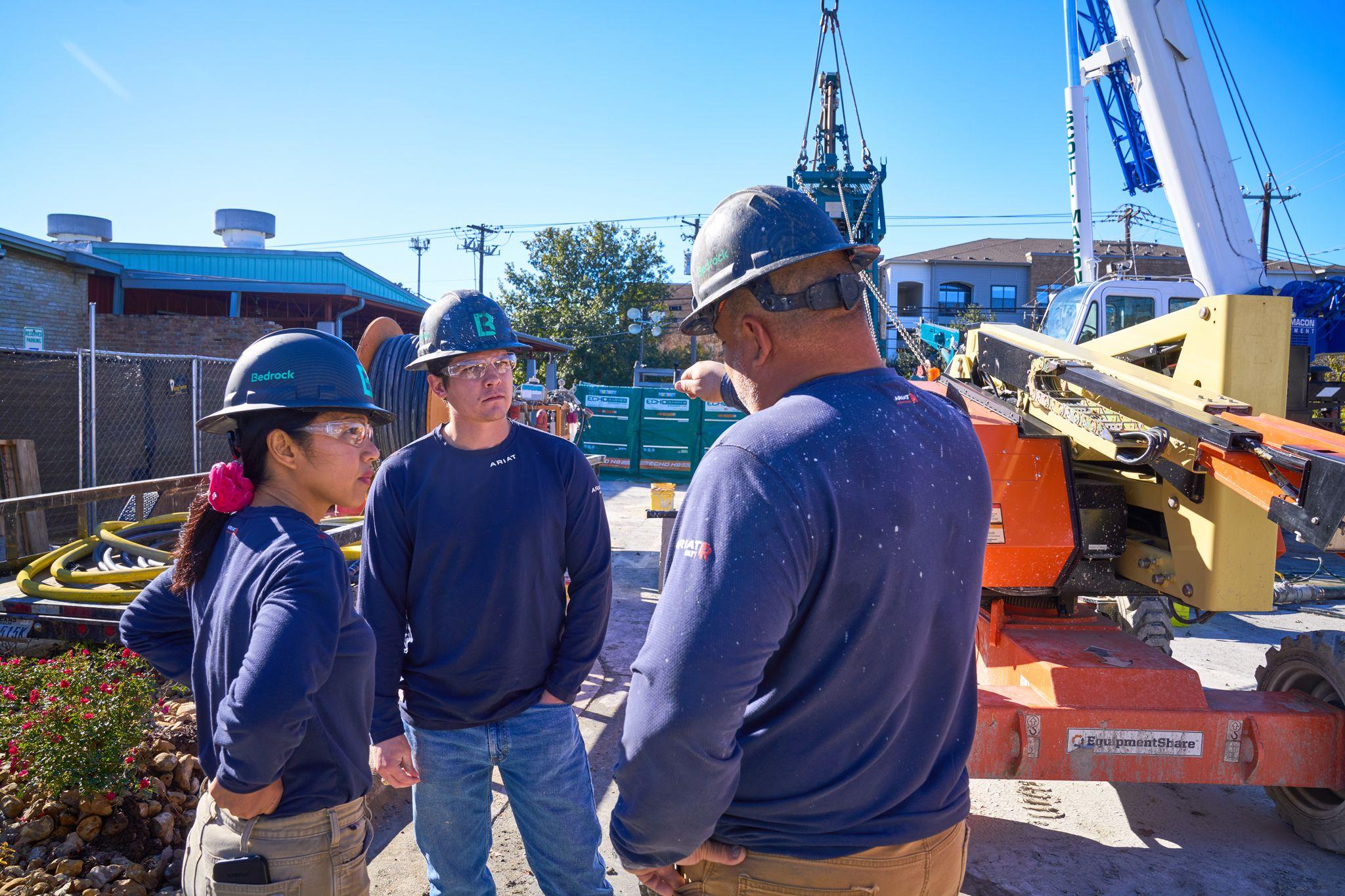 Crew in hard hats talking on a job site with a crane and equipment behind them — Industrial photography, Austin Crew in hard hats talking on a job site with a crane and equipment behind them