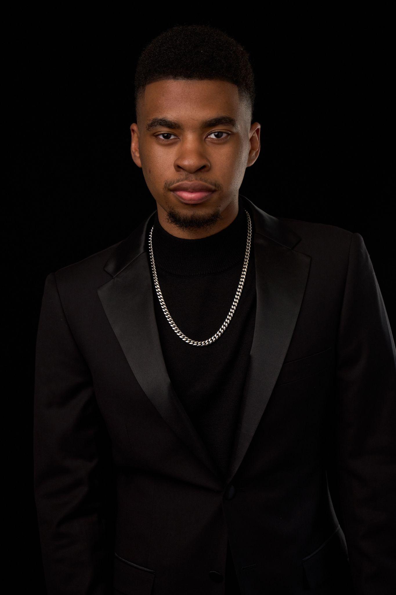 Young man in a black tuxedo and silver chain against a dark studio background — Headshot photography, Austin A young man in a black tuxedo and silver chain against a dark studio background.