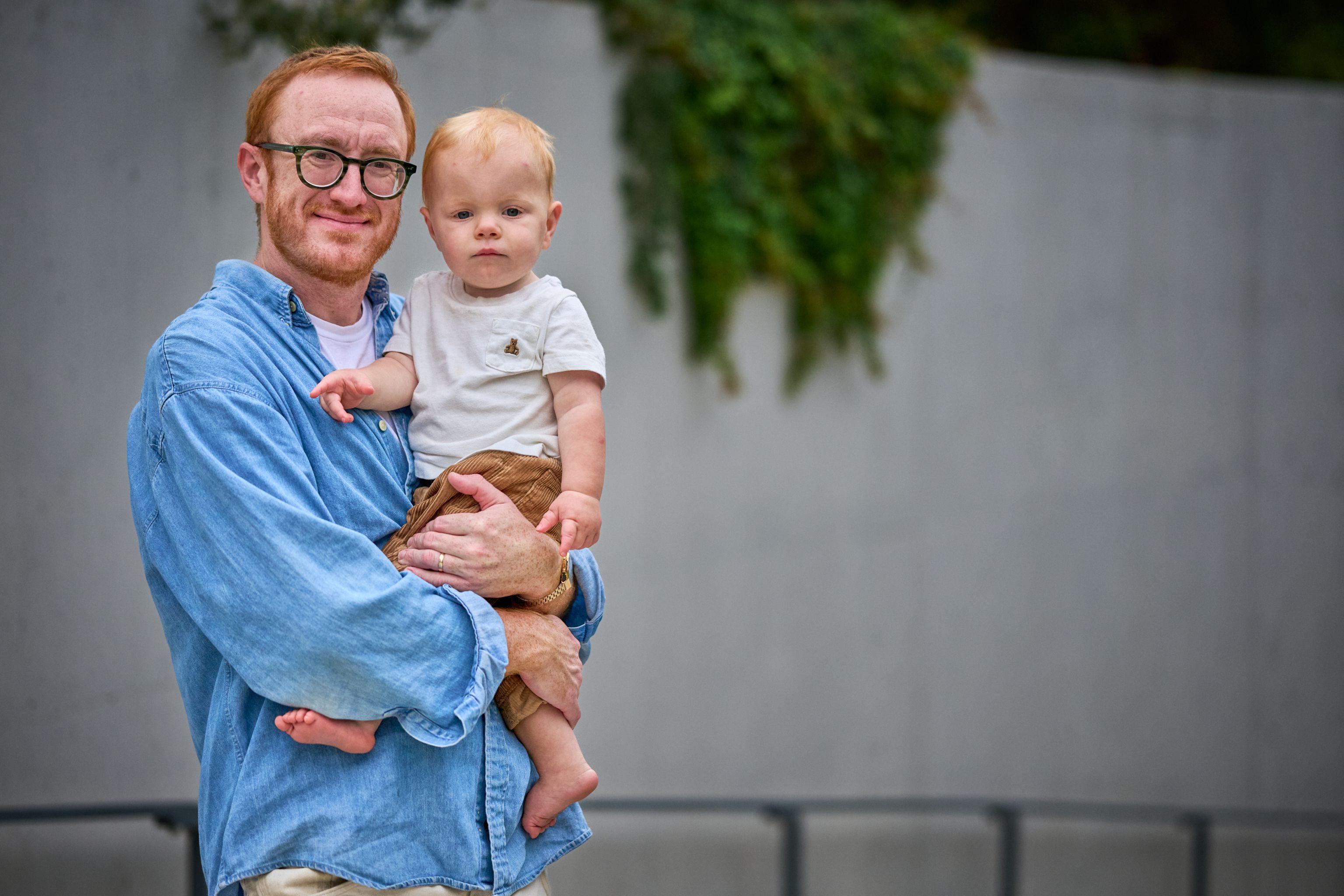 Father holding his baby in front of a concrete wall hung with greenery — Waterloo Park photography, Austin A father holding his baby in front of a concrete wall hung with greenery.