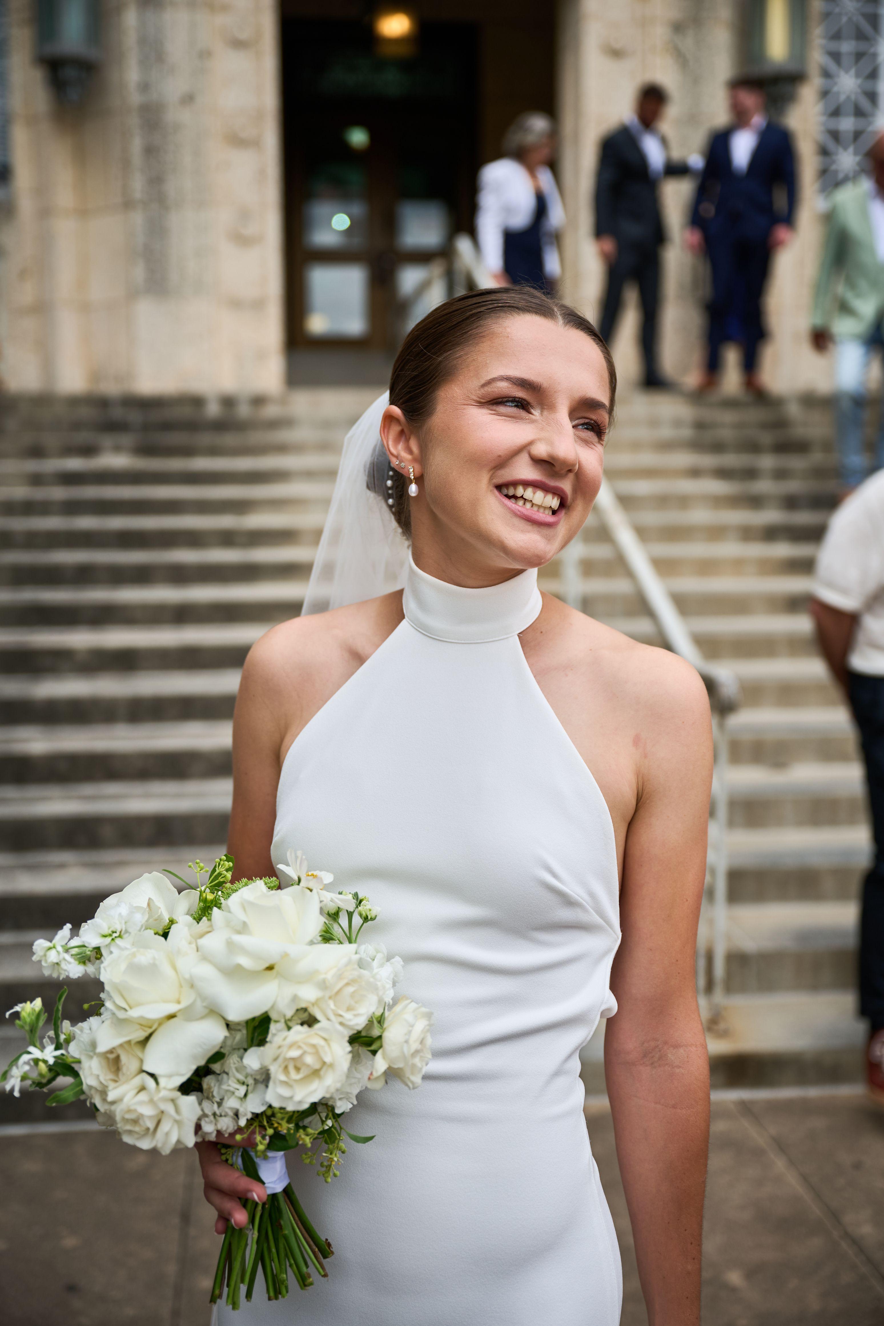 Bride on the courthouse steps holding a white bouquet, guests blurred — Elopements photography, Austin A bride on the courthouse steps holding a white bouquet, guests blurred behind.