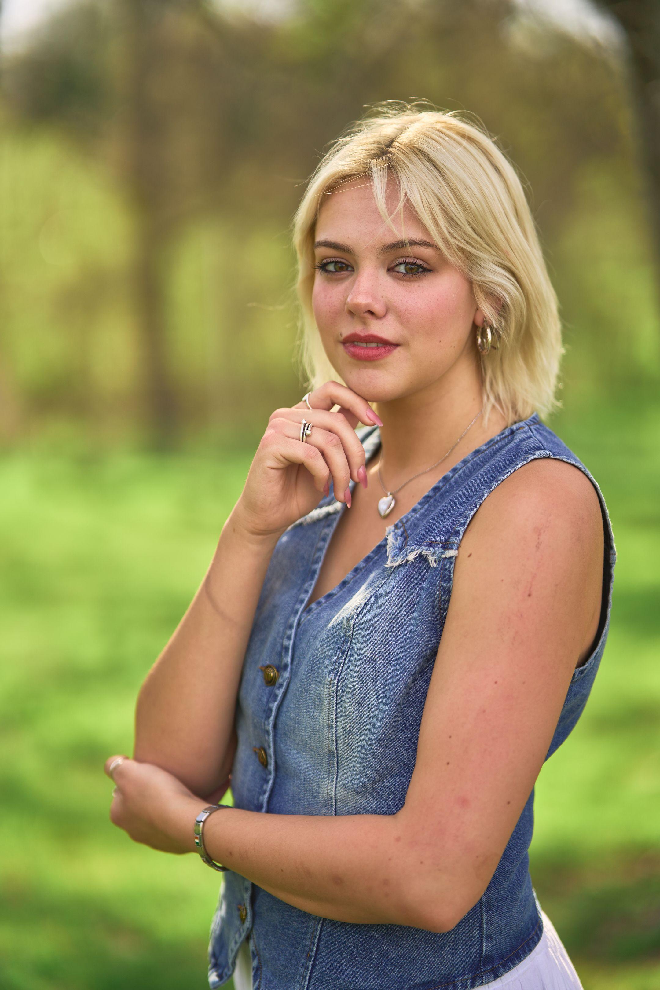 Woman in a denim vest standing in green foliage — Headshot photography, Austin A woman in a denim vest standing in green foliage.