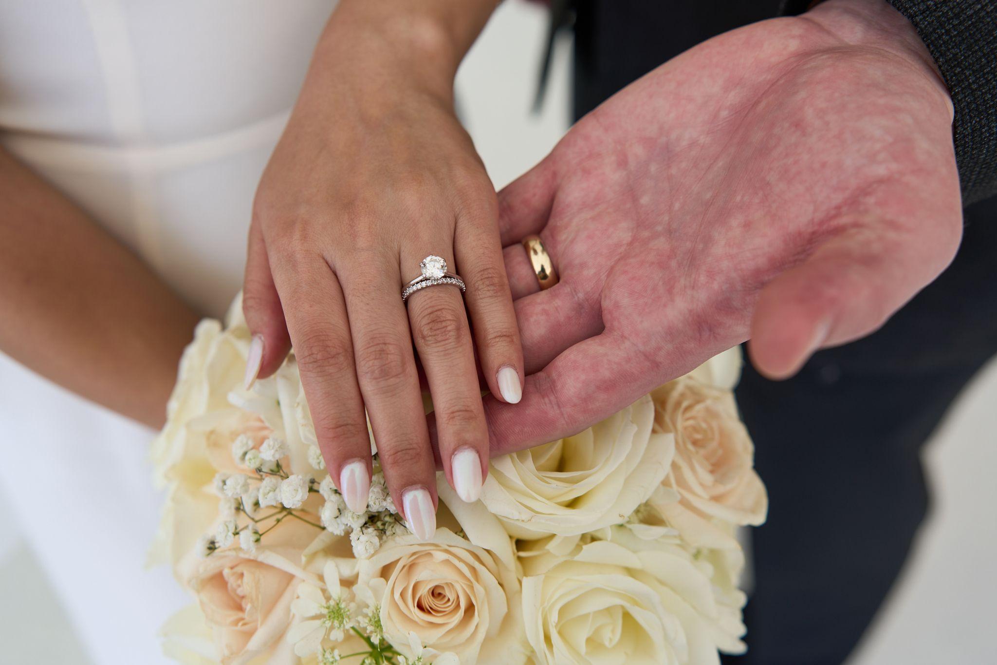 Couple's hands resting on white roses, both wedding bands and an engagement ring visible — Elopements photography, Austin The couple's hands resting on white roses, both wedding bands and an engagement ring visible.