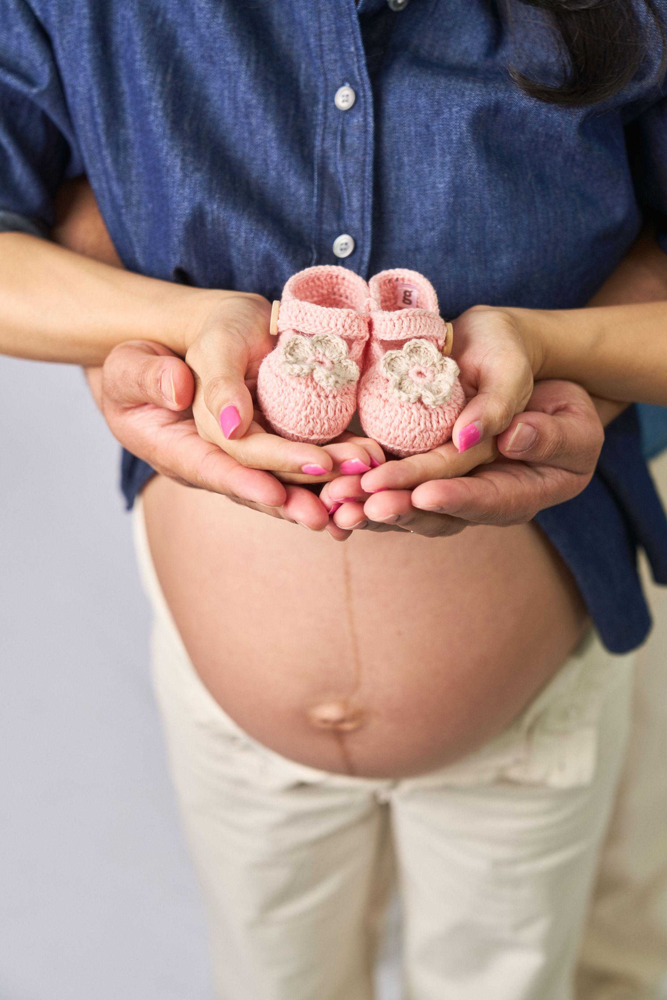 Parents' hands holding tiny pink baby shoes over a belly — Maternity photography, Austin Parents' hands holding tiny pink baby shoes over a belly