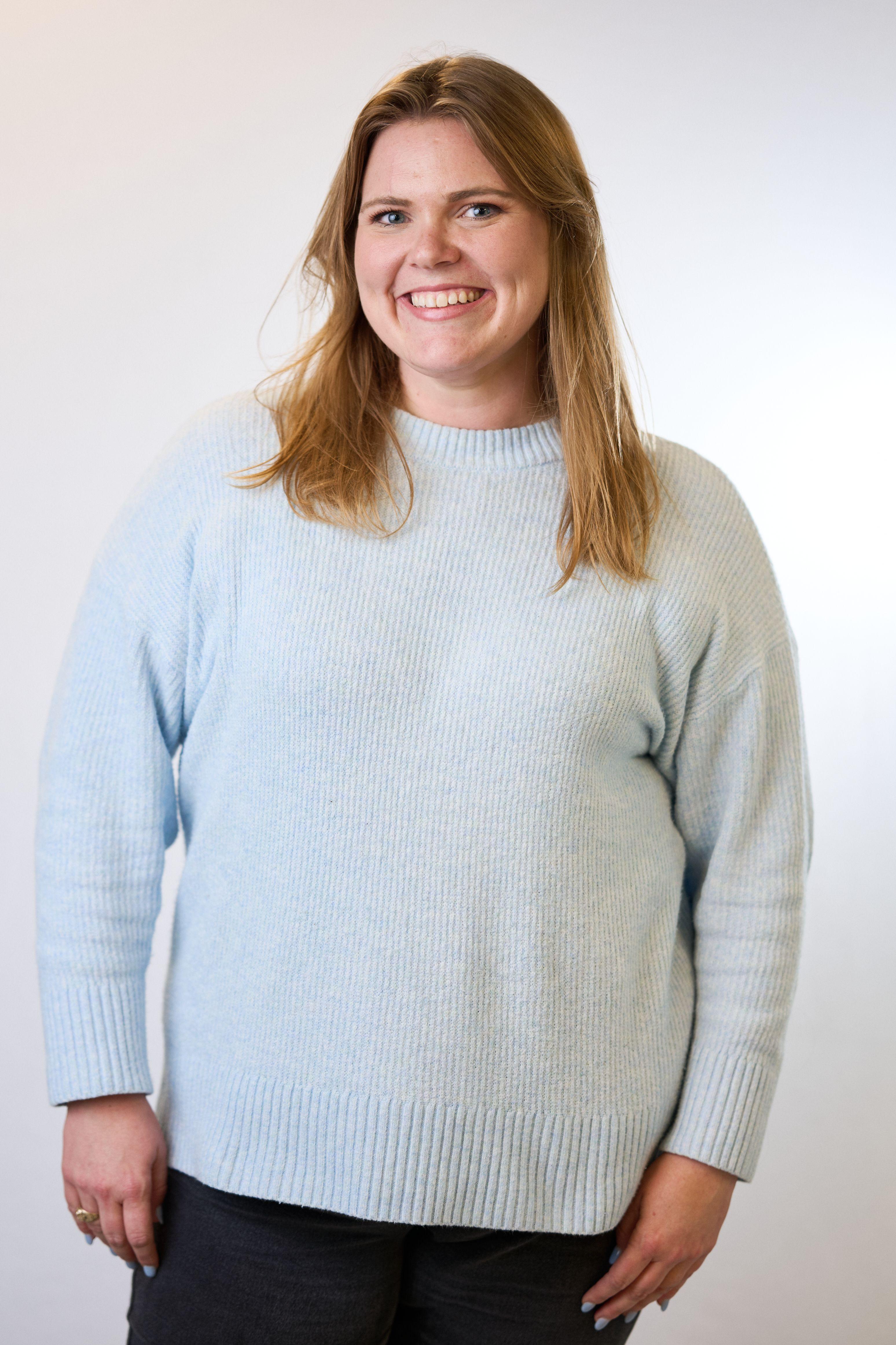 Woman in a pale blue sweater smiling against a white studio backdrop — Headshot photography, Austin A woman in a pale blue sweater smiling against a white studio backdrop.