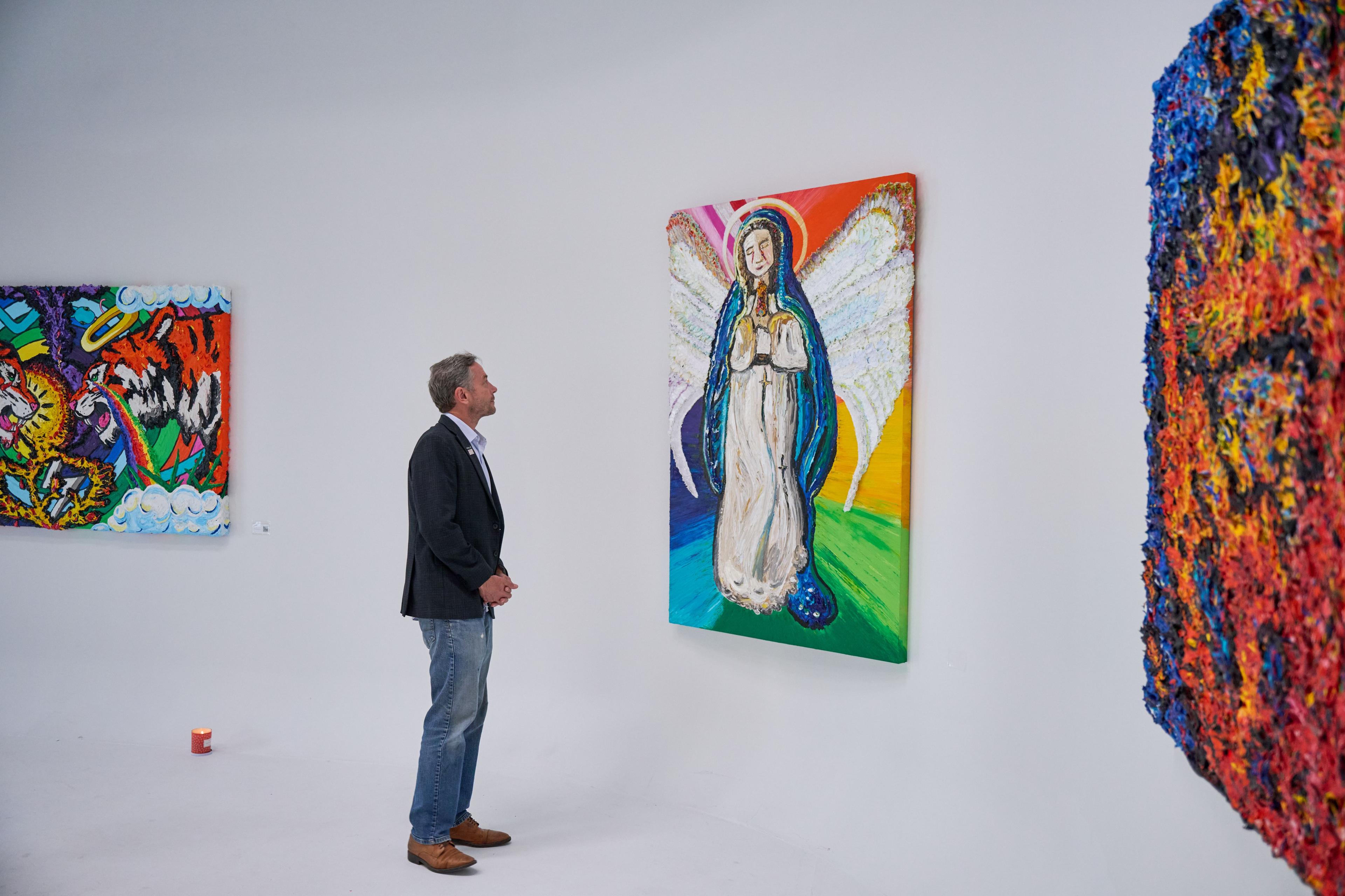 Visitor viewing a large rainbow religious portrait on a gallery wall — Brand activation photography, Austin A visitor viewing a large rainbow religious portrait on a gallery wall.