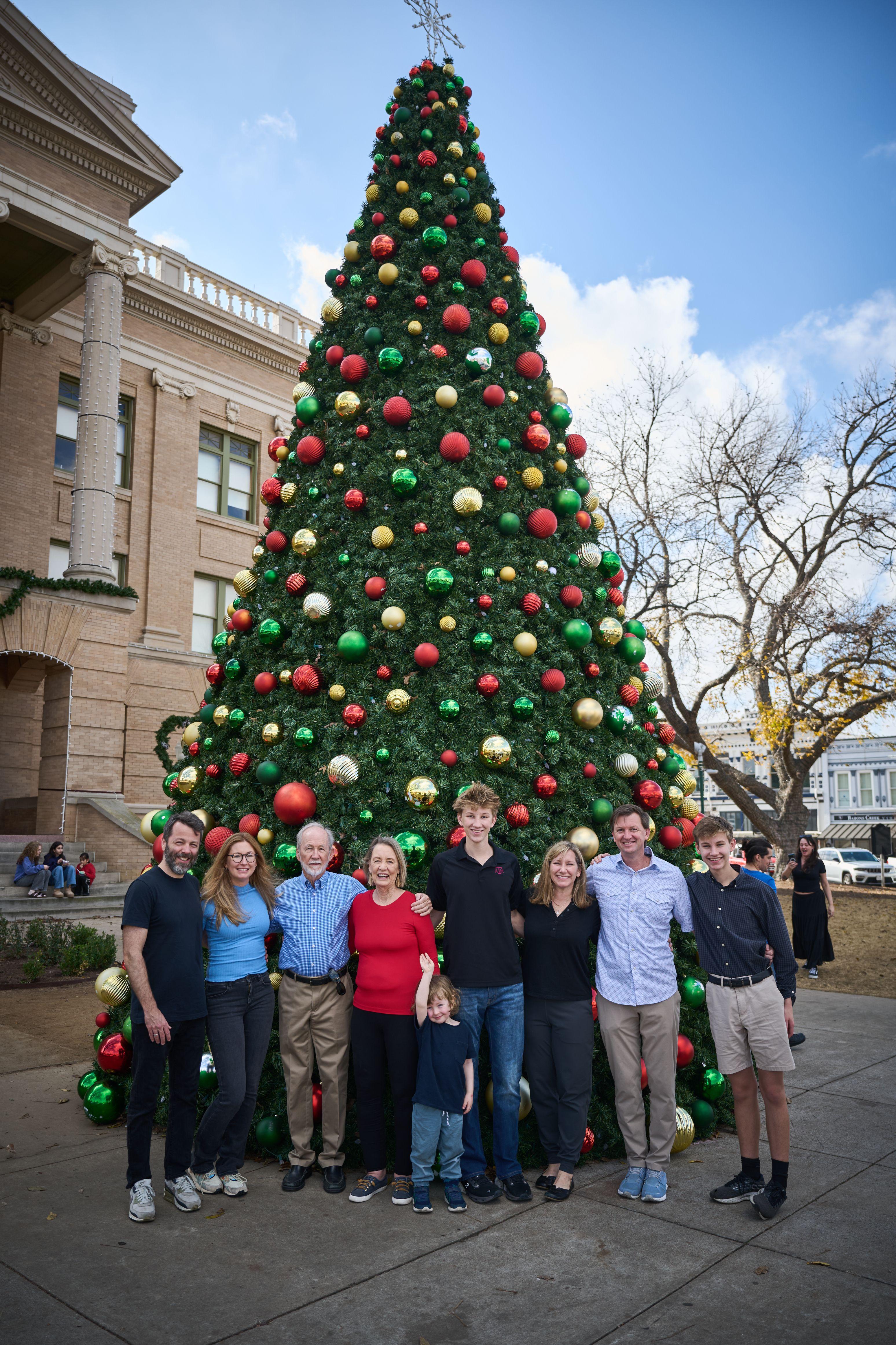Large family posed in front of a giant baubled Christmas tree outside a limestone courthouse — Seasonal Christmas & Fall photography, Austin A large family posed in front of a giant baubled Christmas tree outside a limestone courthouse.
