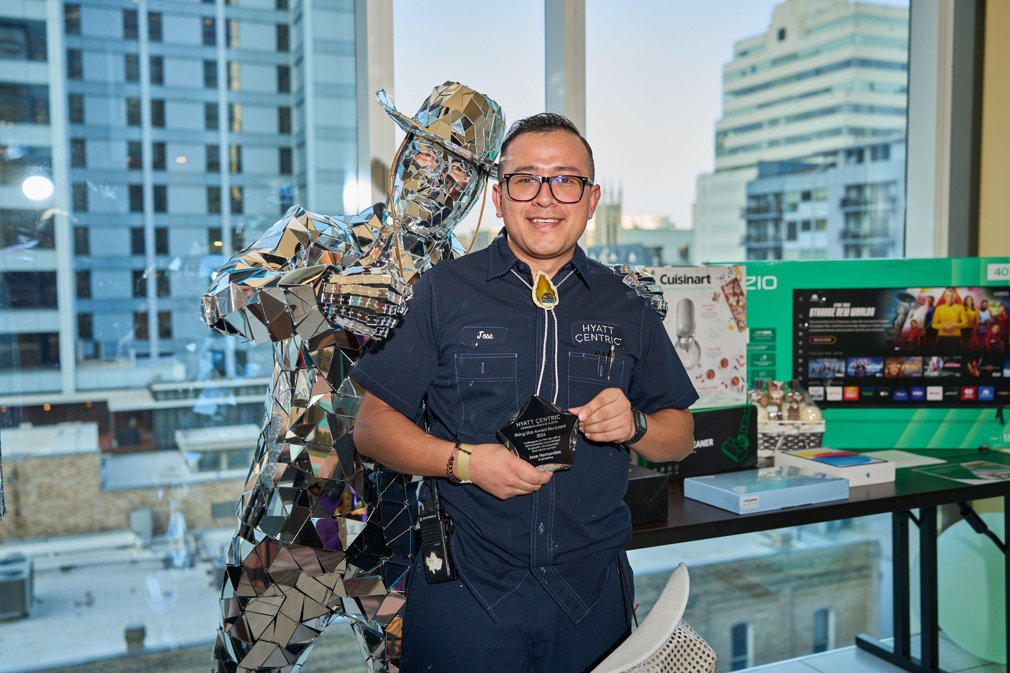 Artist in a denim shirt standing beside a large mirrored mosaic sculpture — Brand activation photography, Austin An artist in a denim shirt standing beside a large mirrored mosaic sculpture.