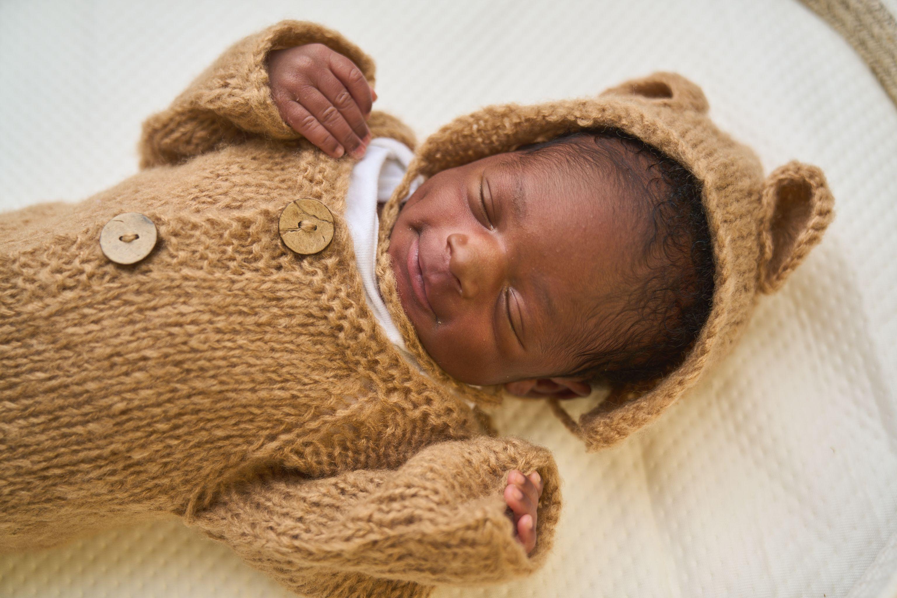 Newborn asleep in a knitted caramel romper and bonnet — Newborn photography, Austin A newborn asleep in a knitted caramel romper and bonnet.