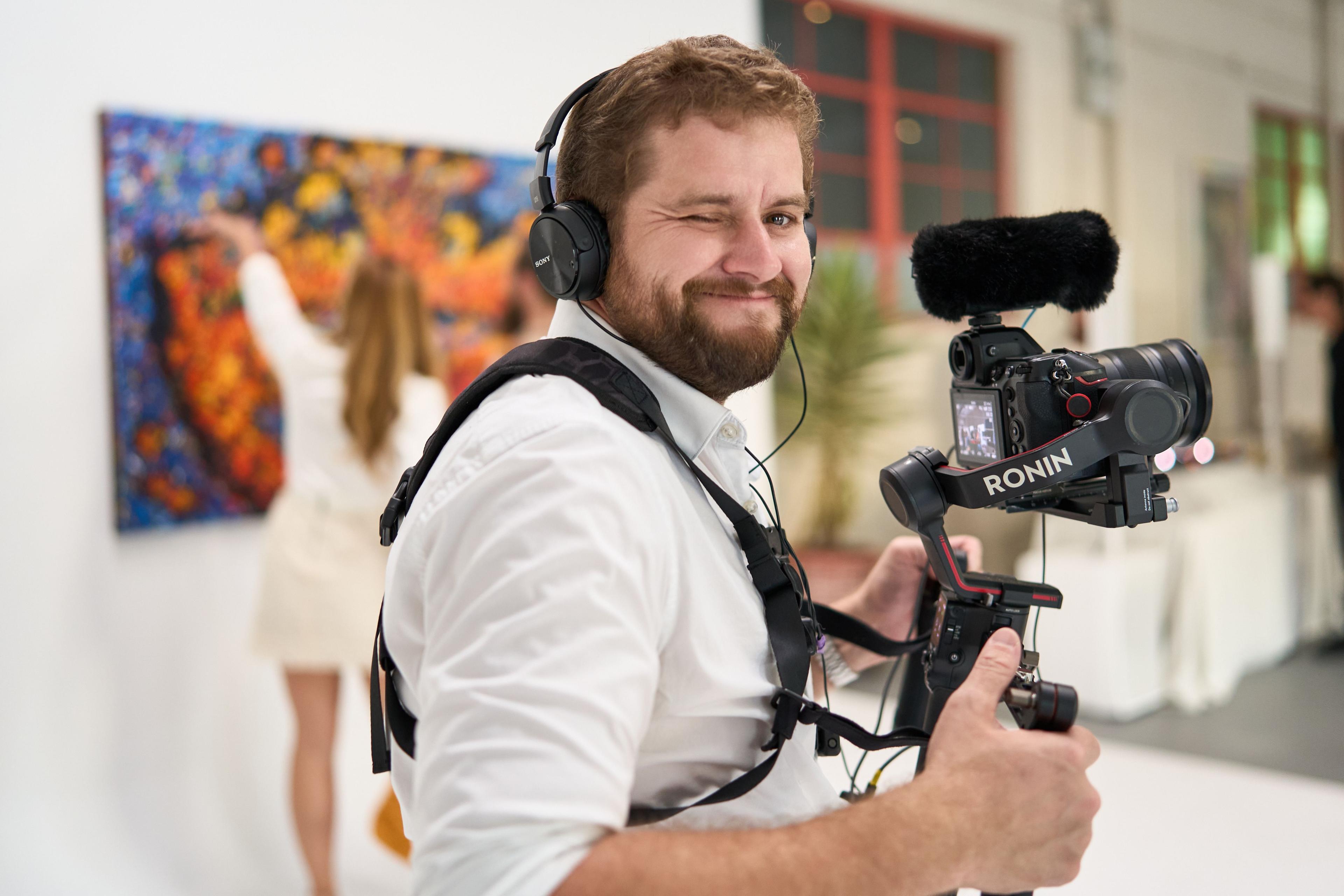 Camera operator in a white shirt and headphones filming with a rig at an indoor event — Production behind-the-scenes, Austin Camera operator in a white shirt and headphones filming with a rig at an indoor event