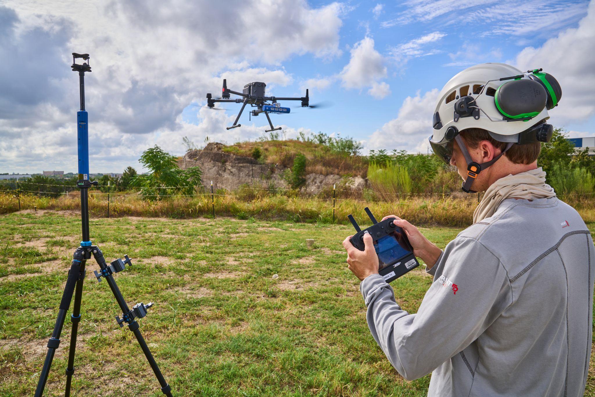 Drone pilot with a handheld controller flying a survey drone over open scrubland — Artwork & archival photography, Austin Drone pilot with a handheld controller flying a survey drone over open scrubland under a bright sky