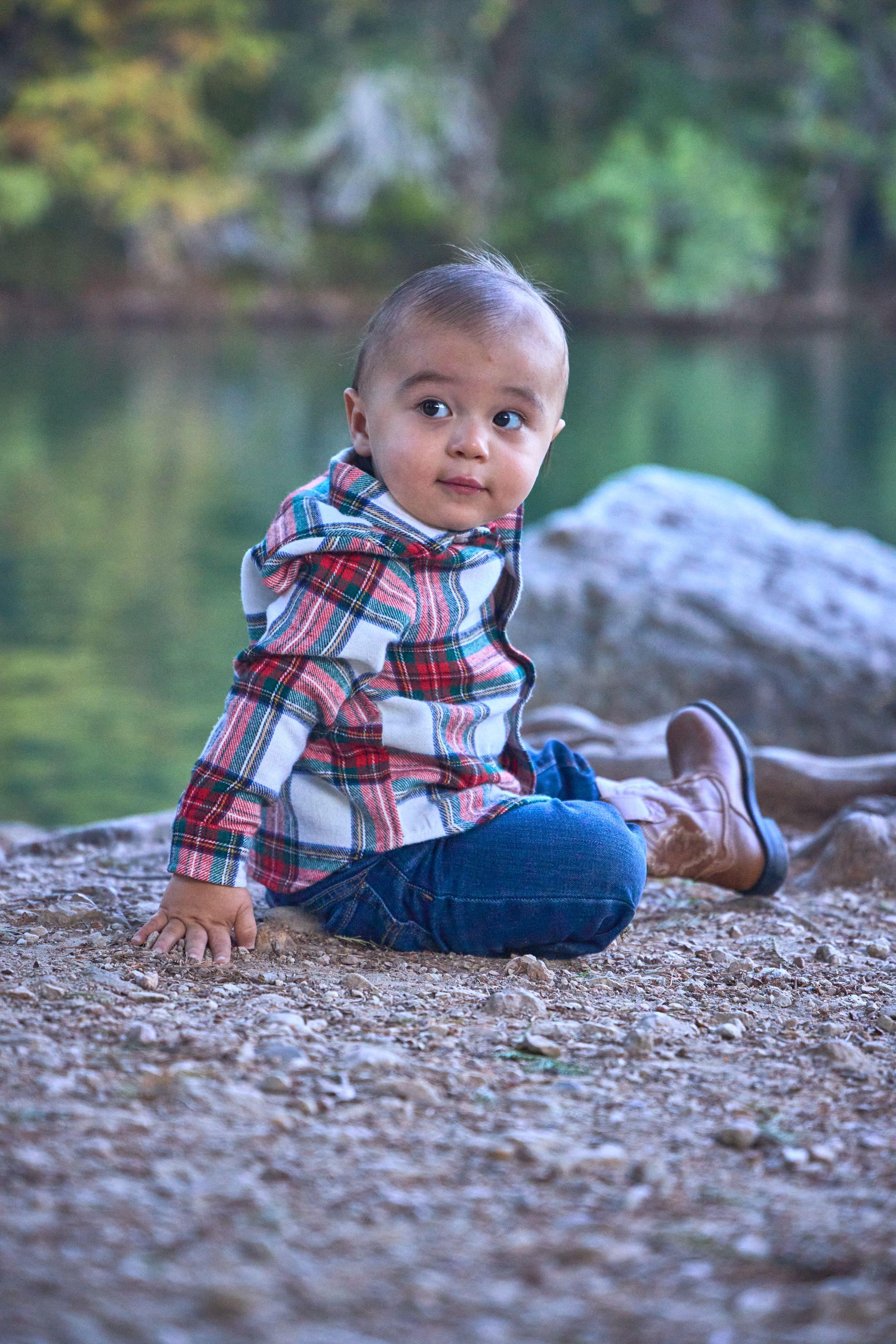Baby in a plaid shirt sitting on the rocks at the edge of the green water at Red Bud Isle — Red Bud Isle photography, Austin A baby in a plaid shirt sitting on the rocks at the edge of the green water at Red Bud Isle