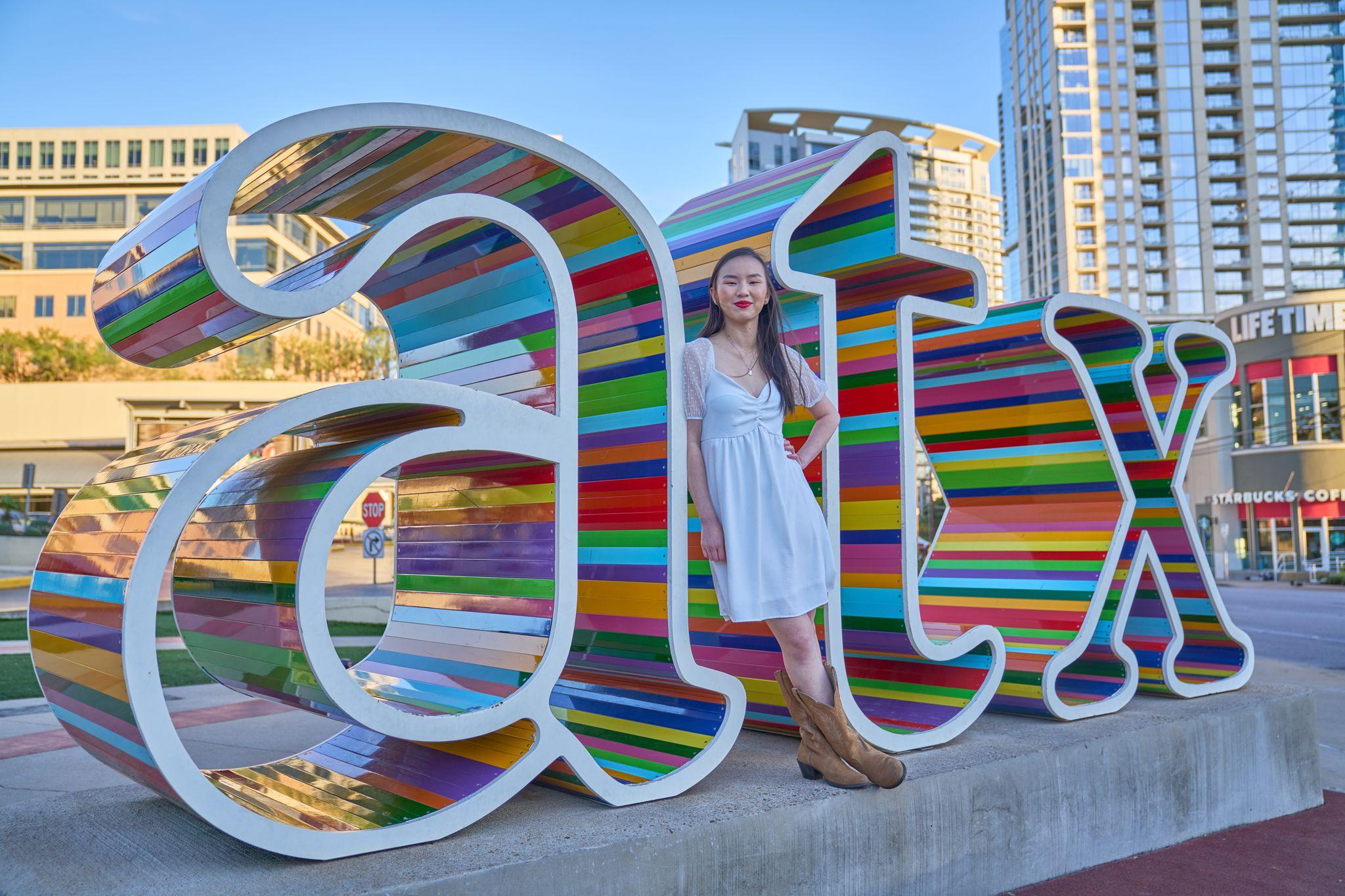 Young woman in a white dress standing in front of the colorful ATX letters sculpture — Downtown Austin photography, Austin A young woman in a white dress standing in front of the colorful ATX letters sculpture.