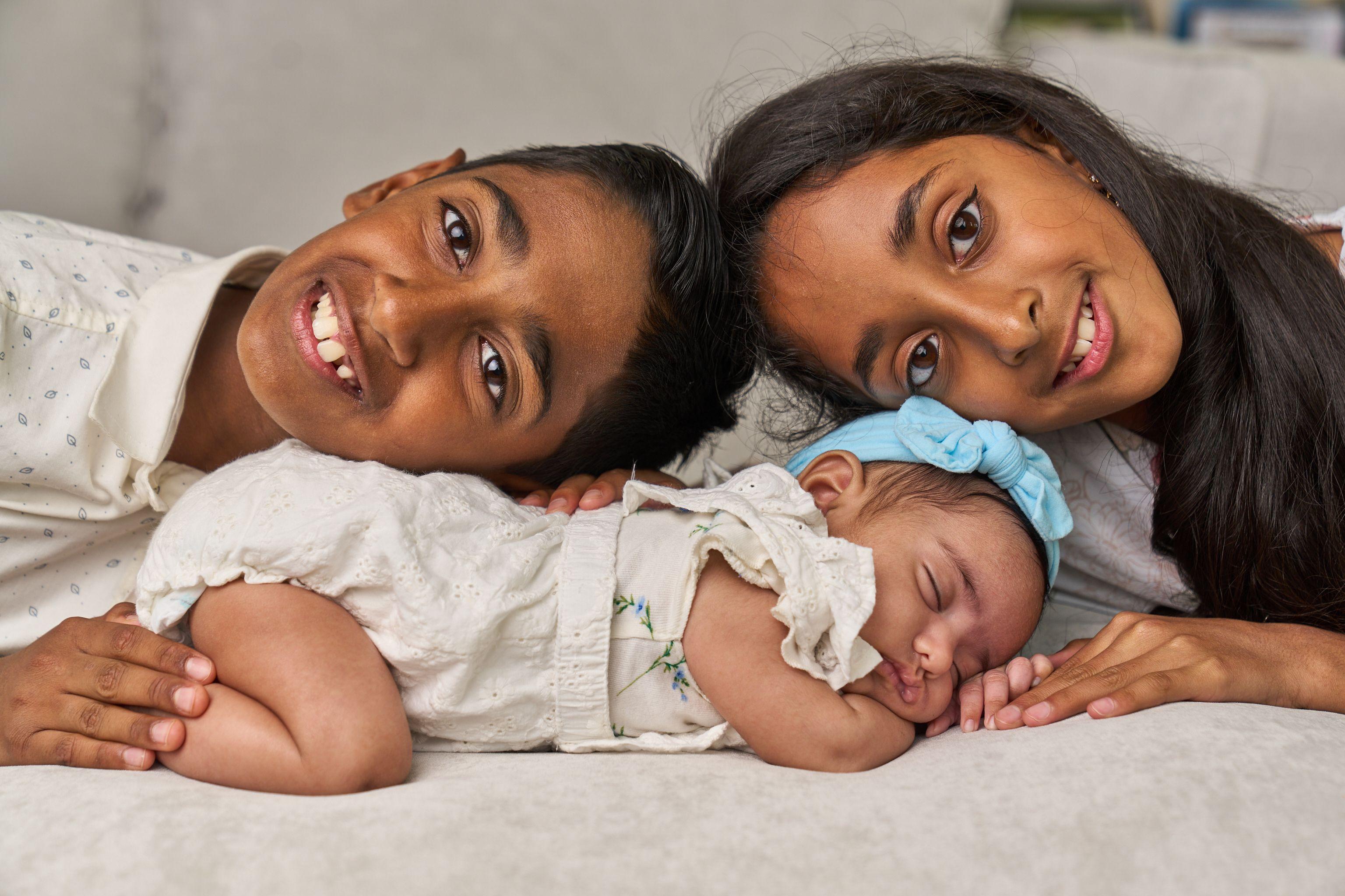 Two older sisters lying head to head beside their sleeping newborn sibling — Newborn photography, Austin Two older sisters lying head to head beside their sleeping newborn sibling.
