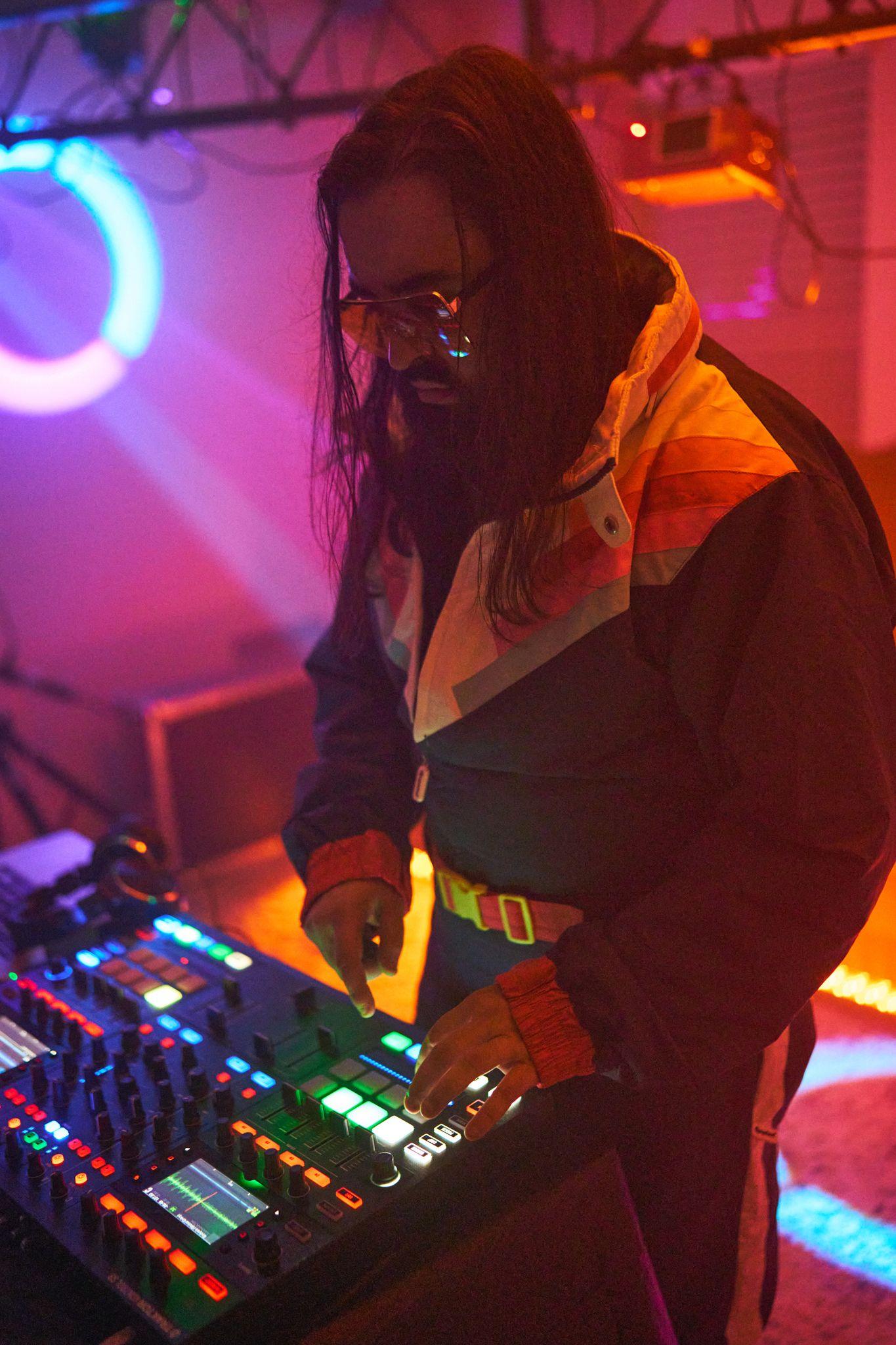 DJ performing behind the decks under pink and orange club lighting — Party & nightlife photography, Austin A DJ performing behind the decks under pink and orange club lighting.