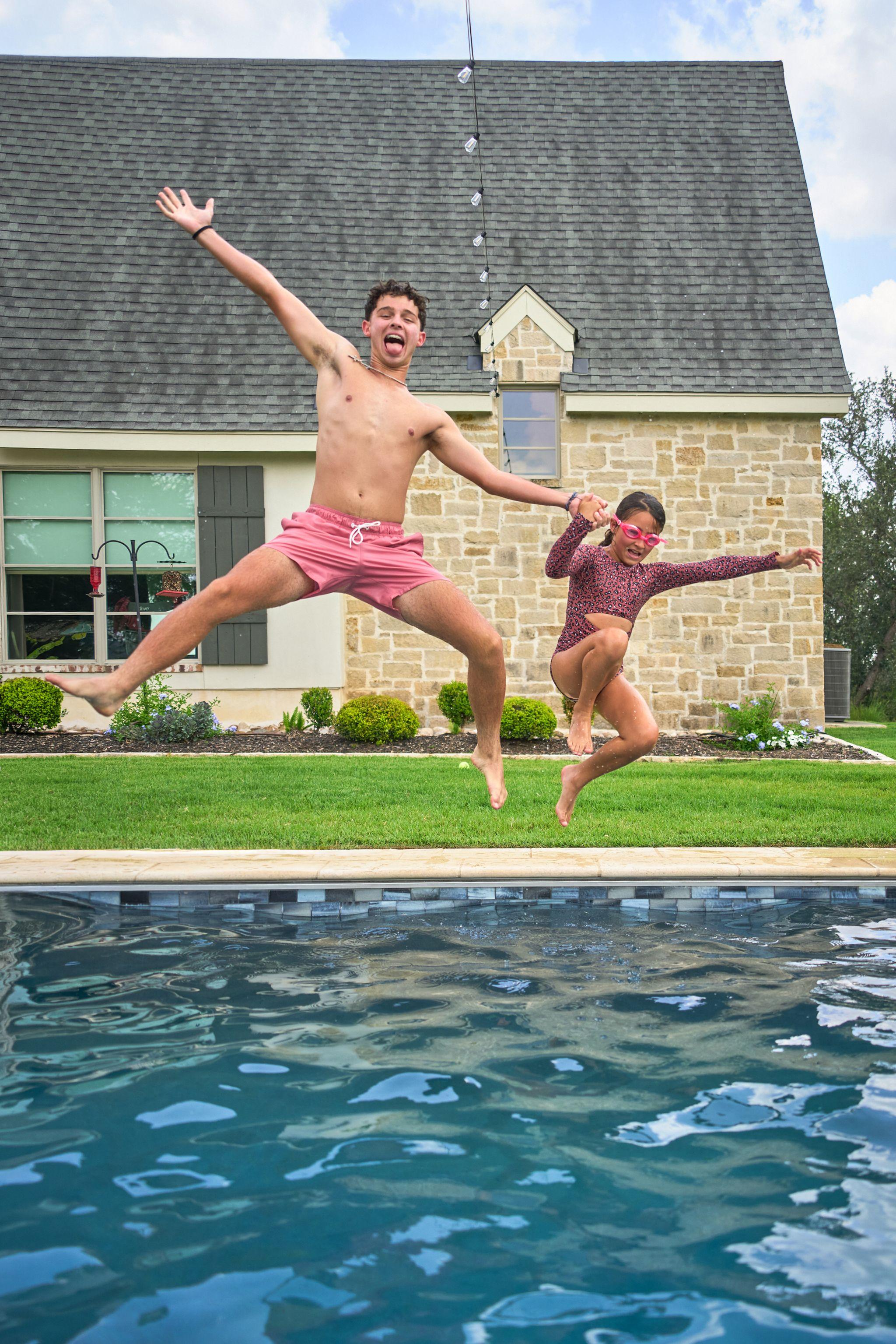 Two boys caught mid-jump over a swimming pool in front of a stone house — Family Portraits photography, Austin Two boys caught mid-jump over a swimming pool in front of a stone house.