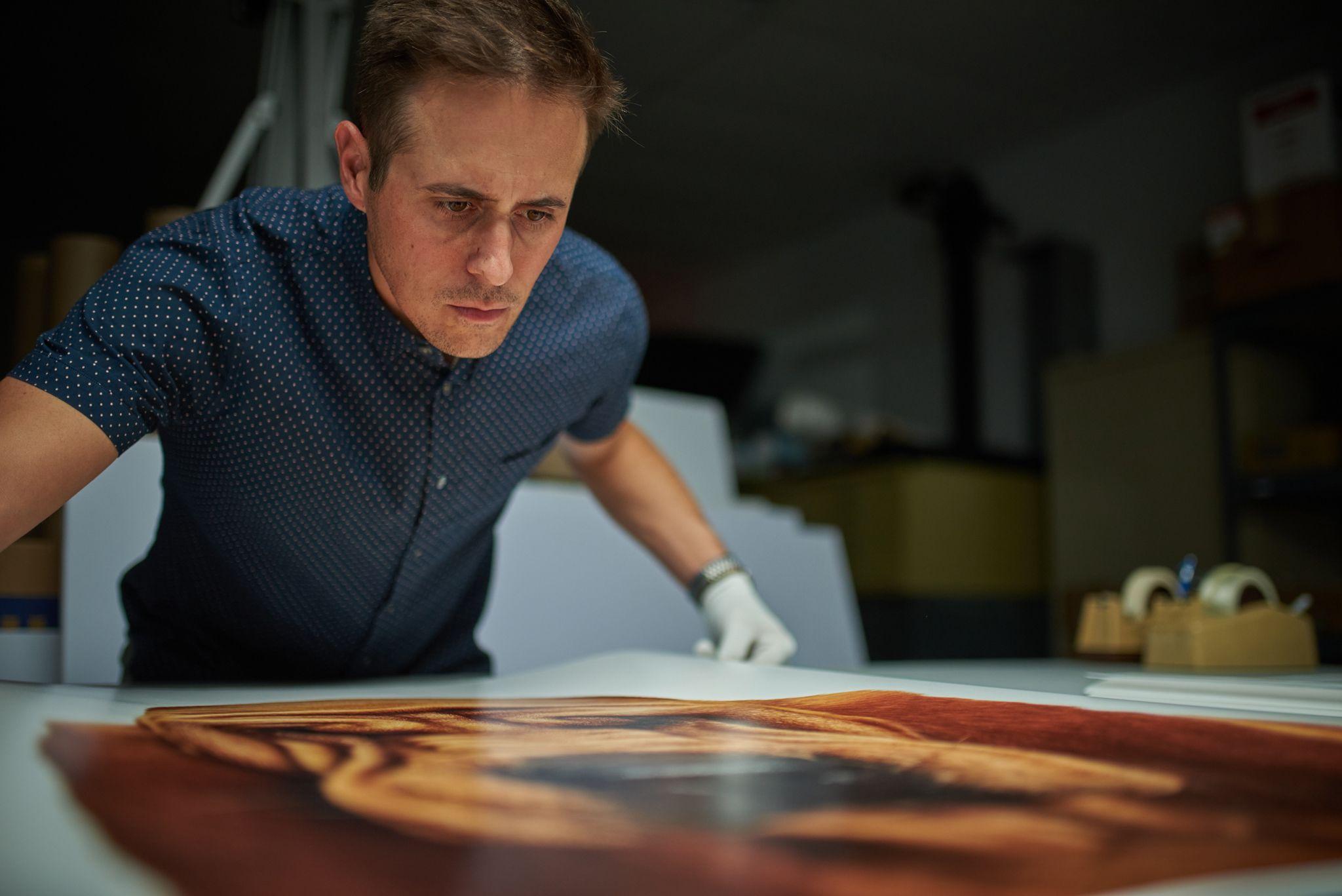 Print technician in white gloves inspecting a large color print on a finishing table — Industrial photography, Austin Print technician in white gloves inspecting a large color print on a finishing table