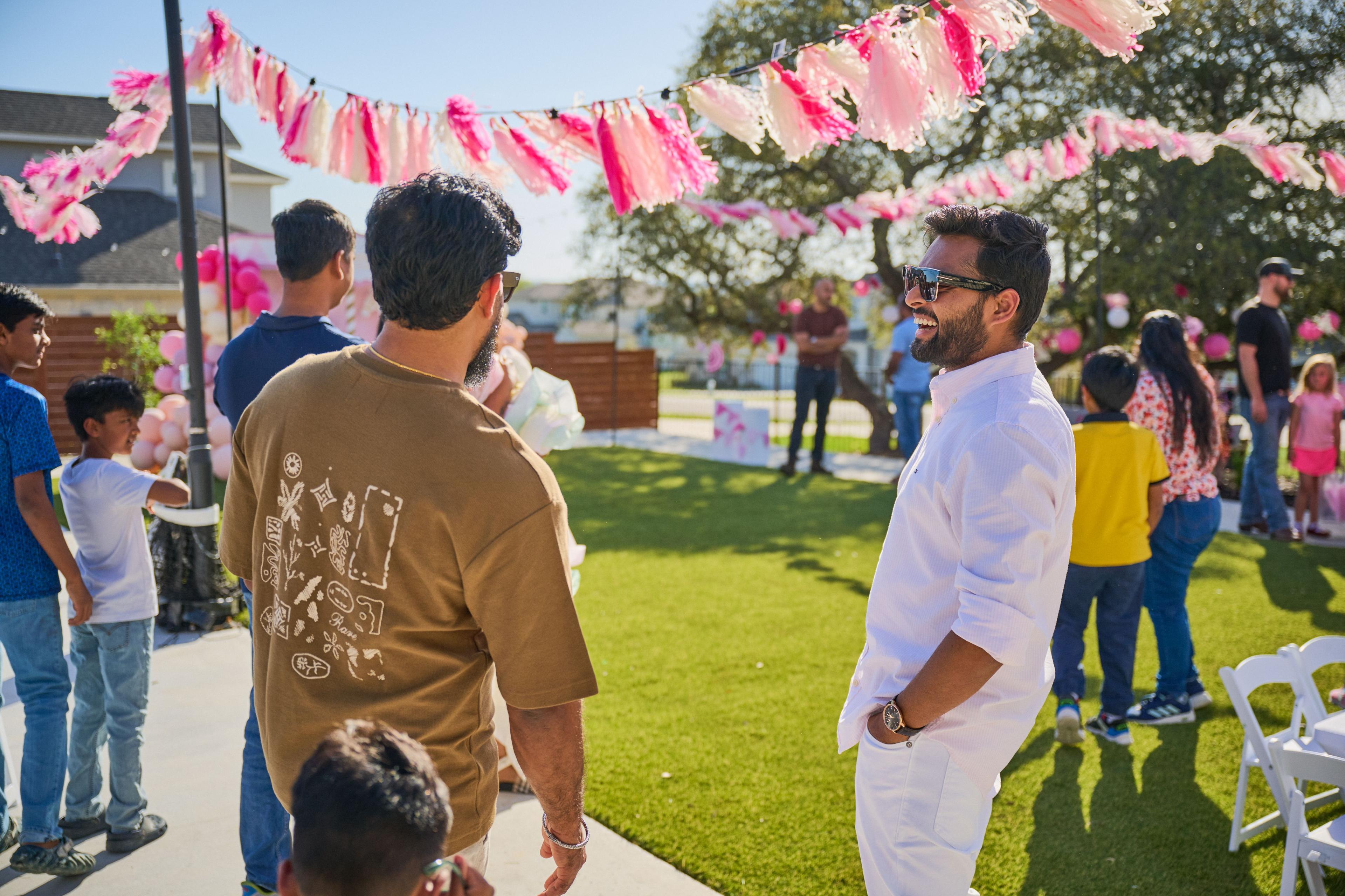 Two men in conversation on the lawn under pink streamers at a family party — Family Parties photography, Austin Two men in conversation on the lawn under pink streamers at a family party.