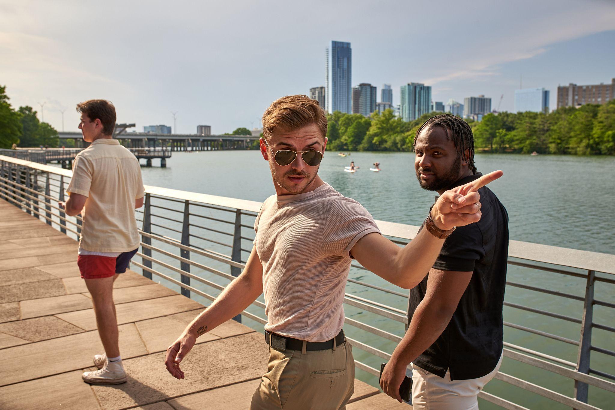 Man in a pink shirt and sunglasses leaning on the boardwalk railing, kayakers on the water — Austin Boardwalk photography, Austin A man in a pink shirt and sunglasses leaning on the boardwalk railing, kayakers on the water and the downtown Austin towers behind him