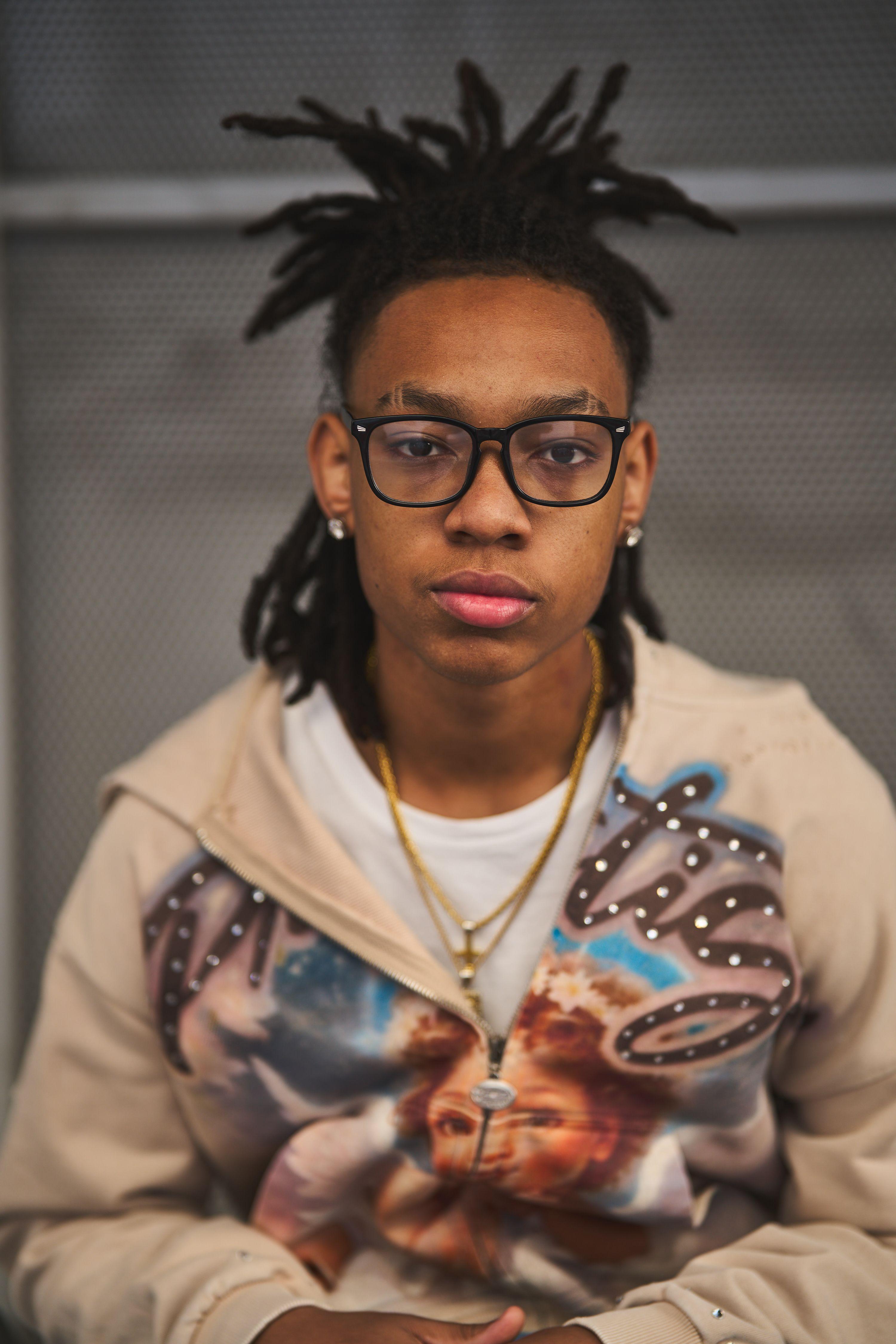 Young man in glasses and a graphic-print hooded sweatshirt with a gold chain, photographed — E-commerce & apparel photography, Austin Young man in glasses and a graphic-print hooded sweatshirt with a gold chain, photographed against a stone building downtown