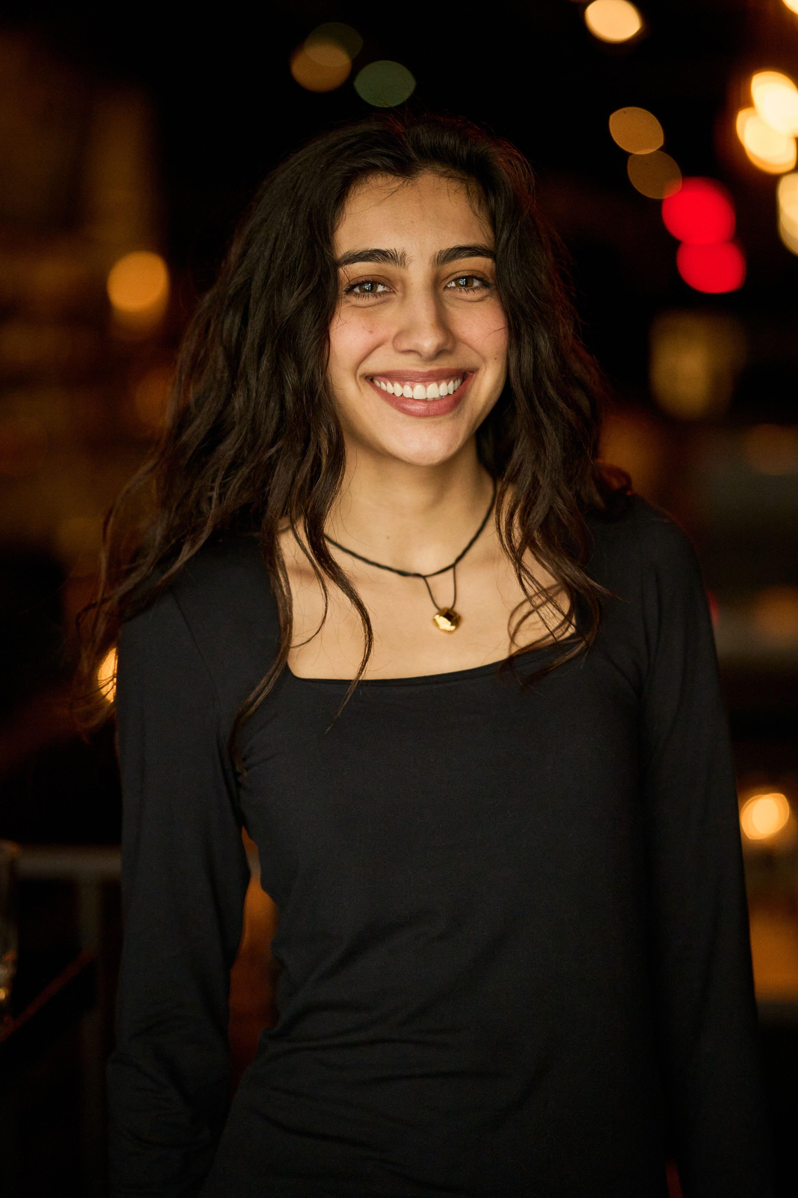 Woman in a black top photographed on a street after dark, warm bar lights out of focus — Business headshots, Austin A woman in a black top photographed on a street after dark, warm bar lights out of focus behind her
