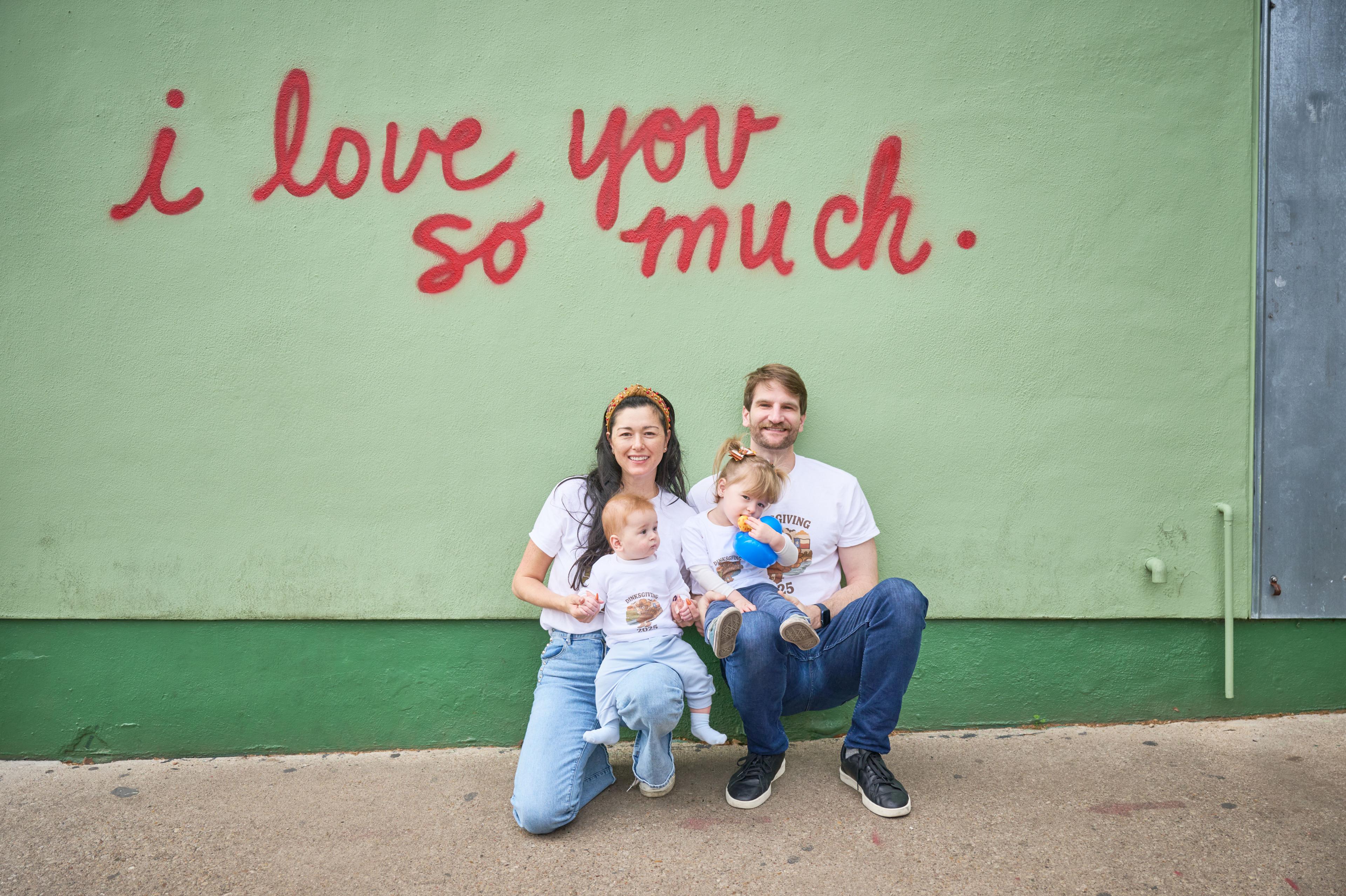Parents crouching with two small children in front of the red script mural — Family Portraits photography, Austin Parents crouching with two small children in front of the red script mural.