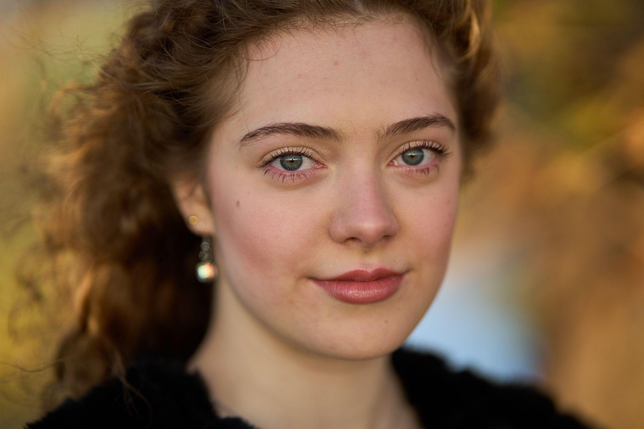 An extreme close portrait of a woman with green eyes and curly auburn hair against autumn bokeh
